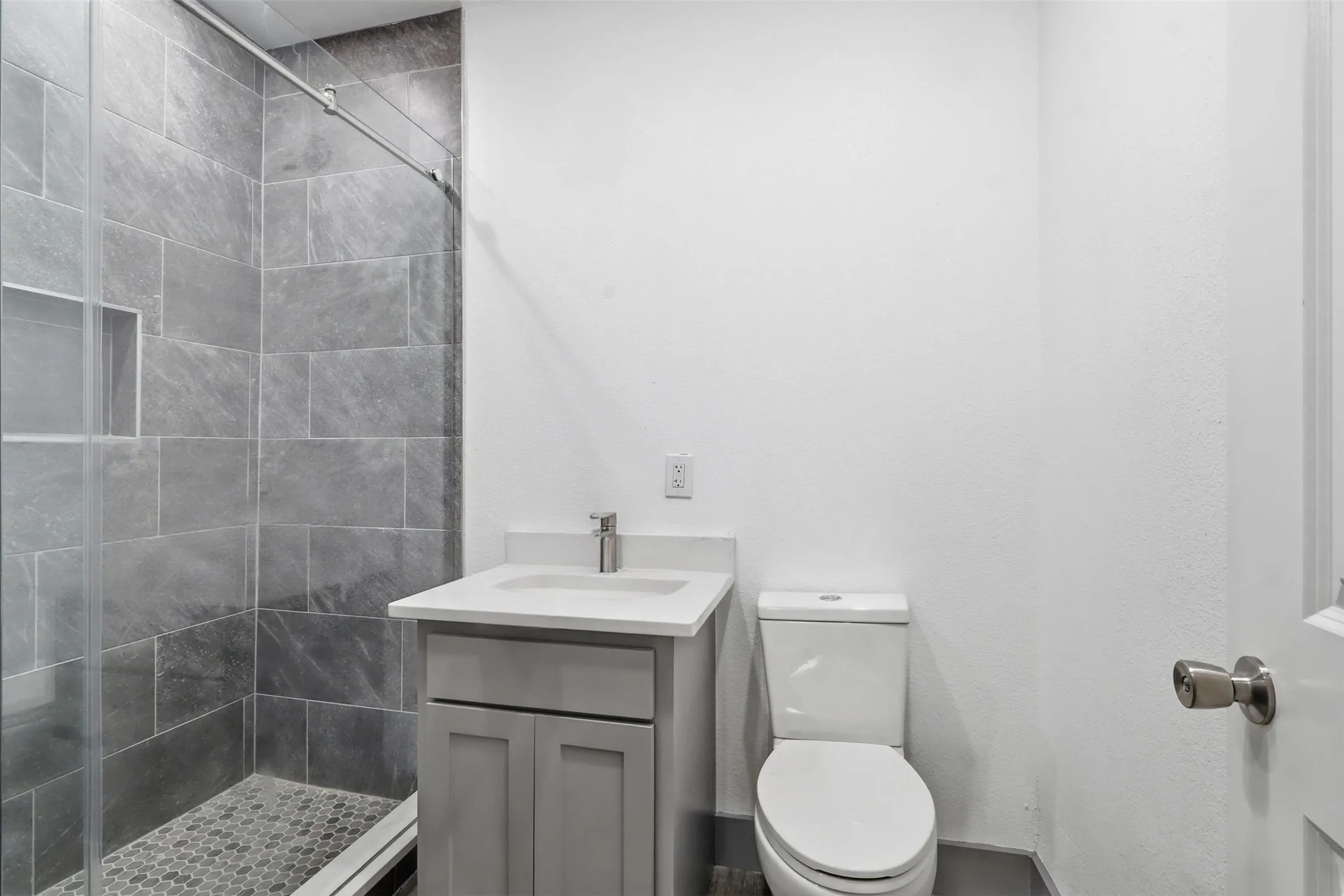 Shower stall with gray rectangular tile surround, glass enclosure, and a built-in niche