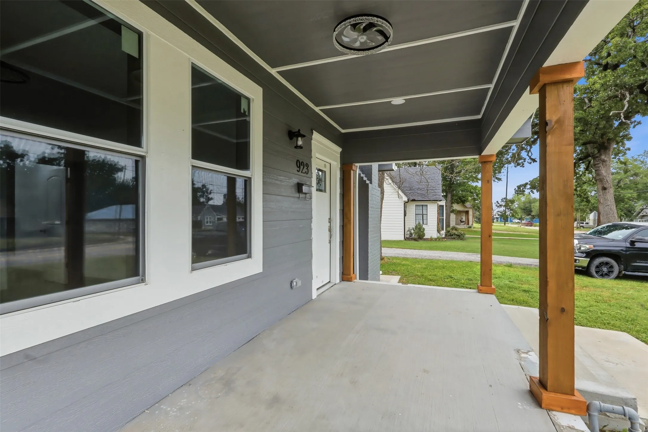 Front porch entry featuring a gray exterior, white trim, natural wood support columns, a concrete slab, and an exterior wall light fixture
