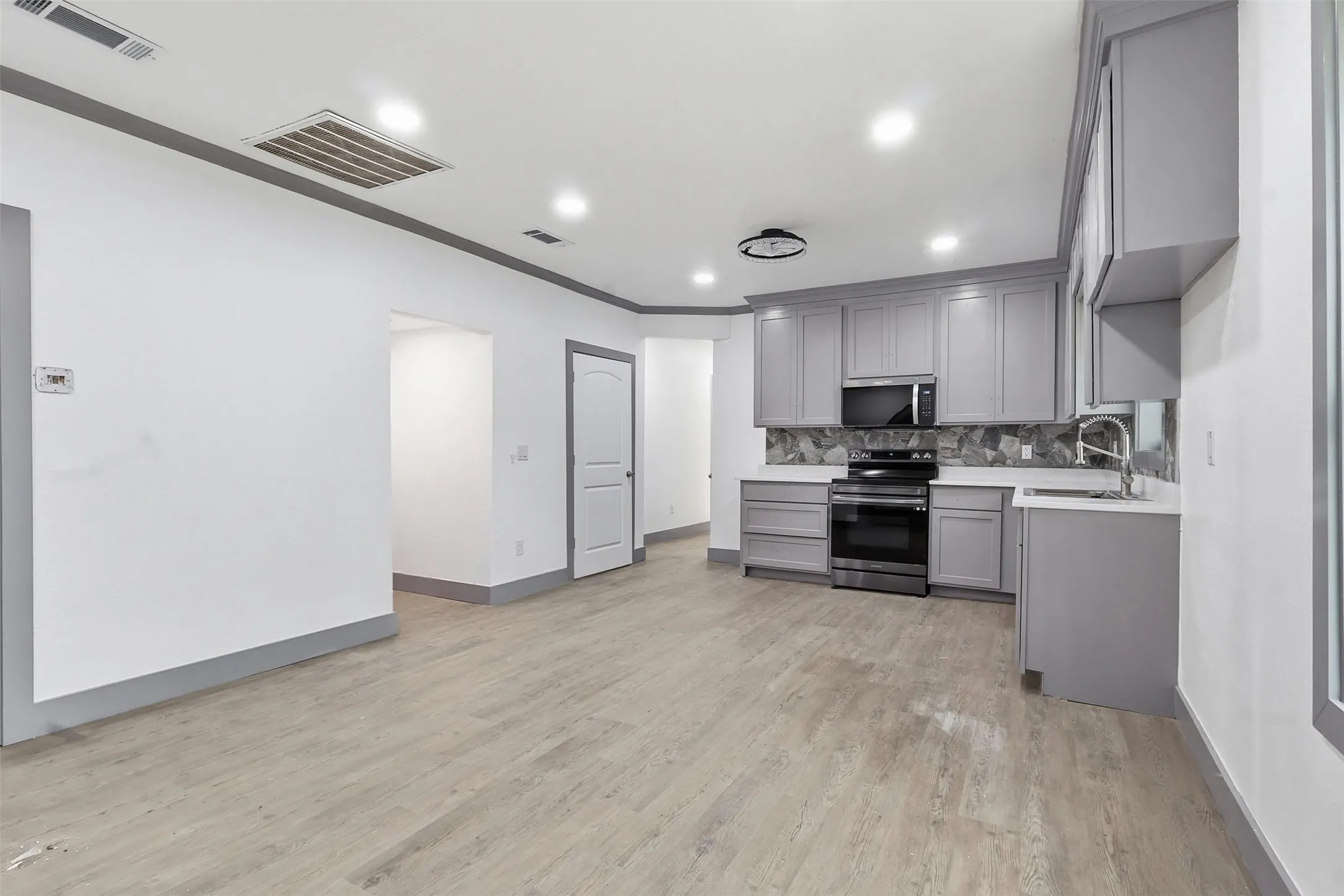 Spacious kitchen featuring light gray cabinetry, white countertops, stainless steel appliances, a unique geometric backsplash, and recessed lighting