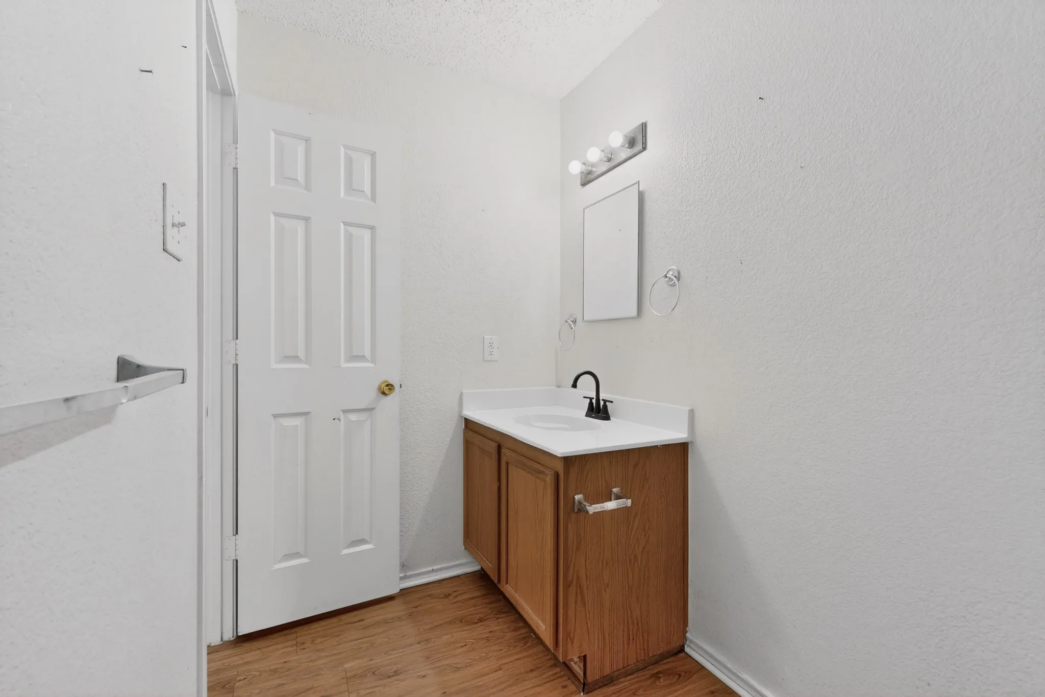 Half bathroom featuring vanity, a textured wall, light wood finished floors, and a textured ceiling