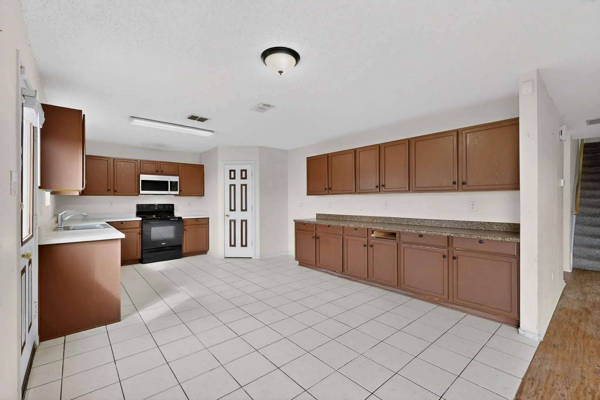 Kitchen featuring black range, white microwave, wood finish cabinetry, light countertops, and light tile patterned flooring