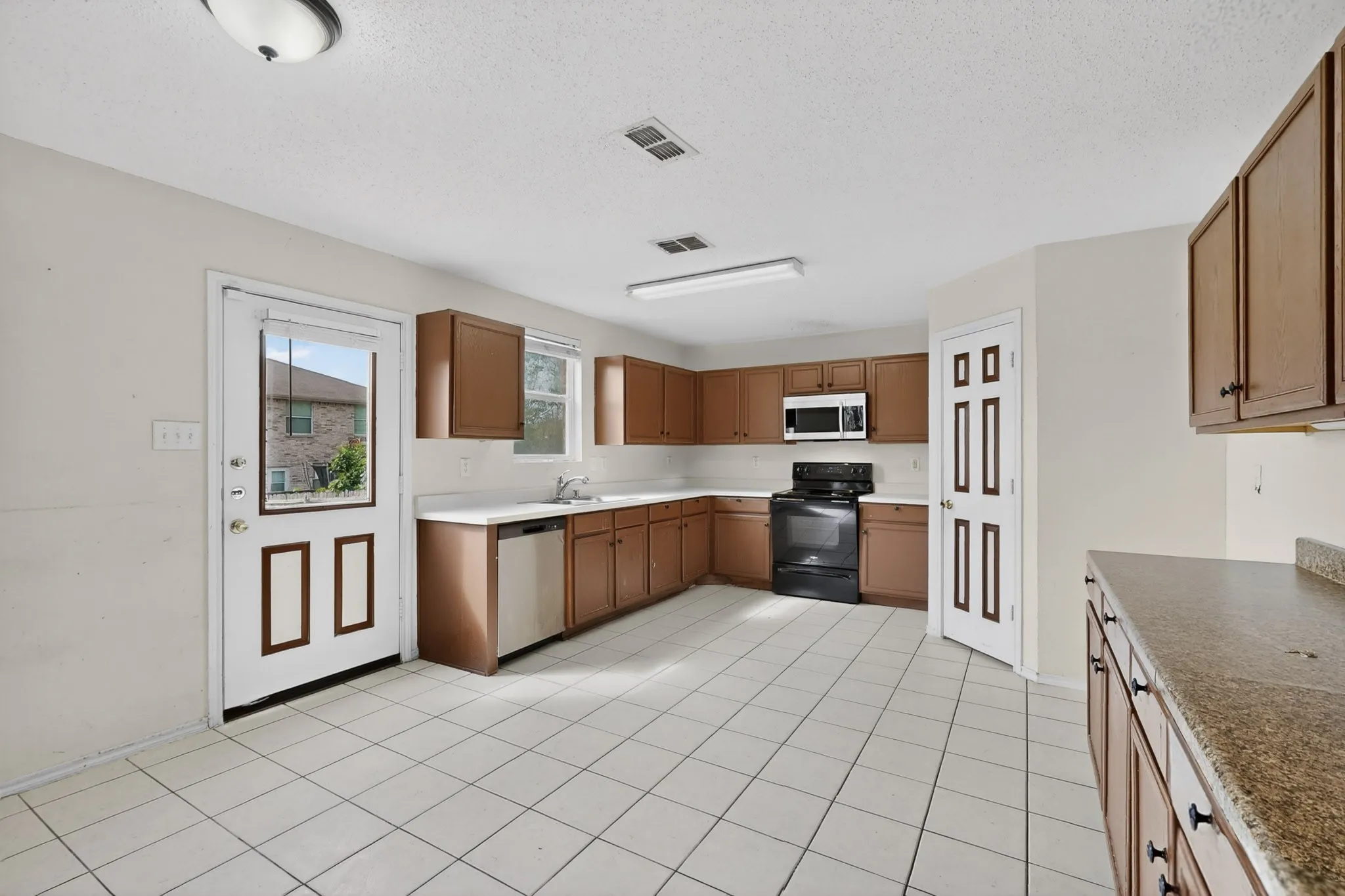 Kitchen featuring black / electric stove, dishwasher, wood finish cabinets, a textured ceiling, and light countertops