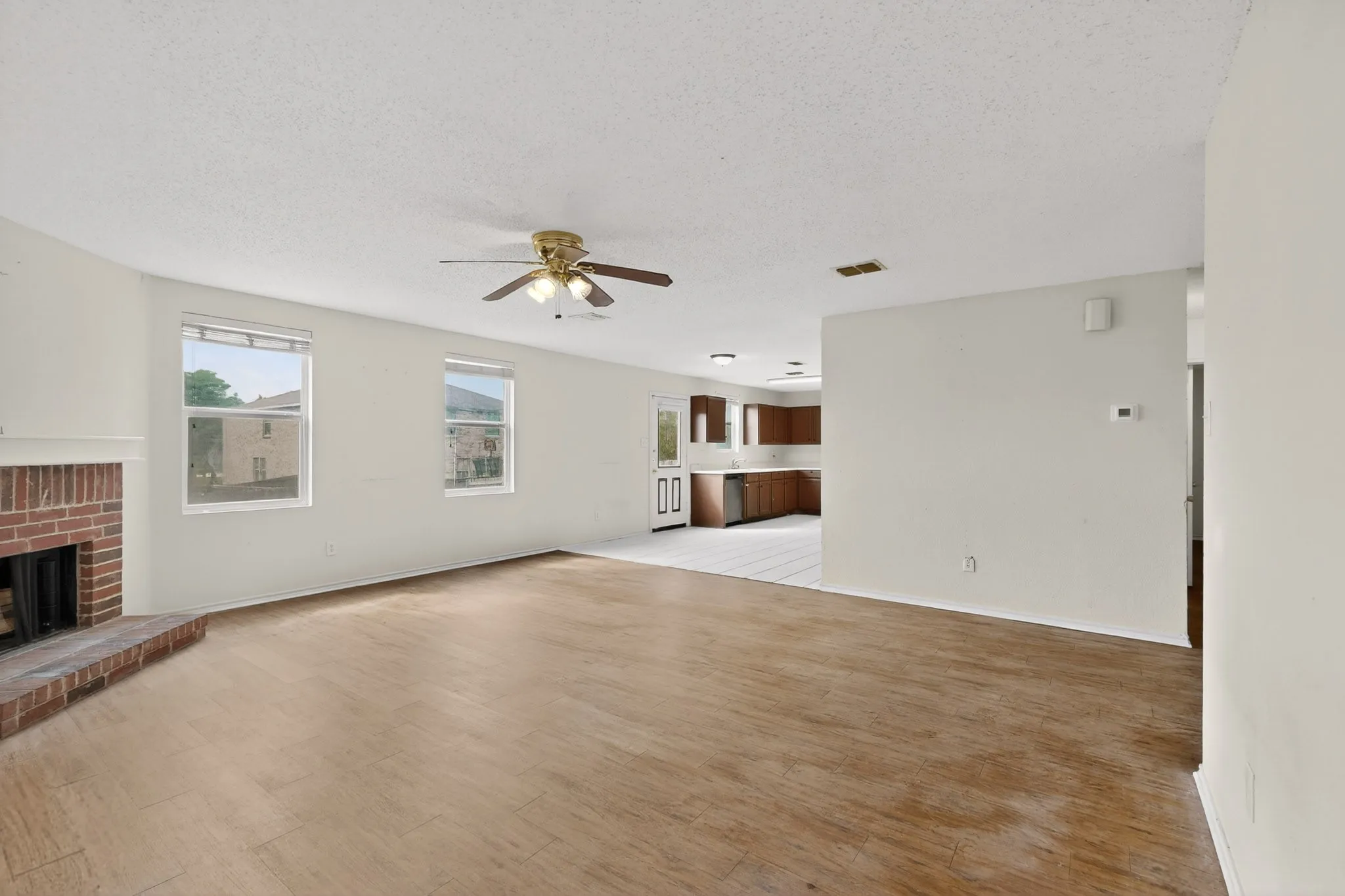 Unfurnished living room featuring a fireplace, a ceiling fan, light wood-type flooring, and a textured ceiling