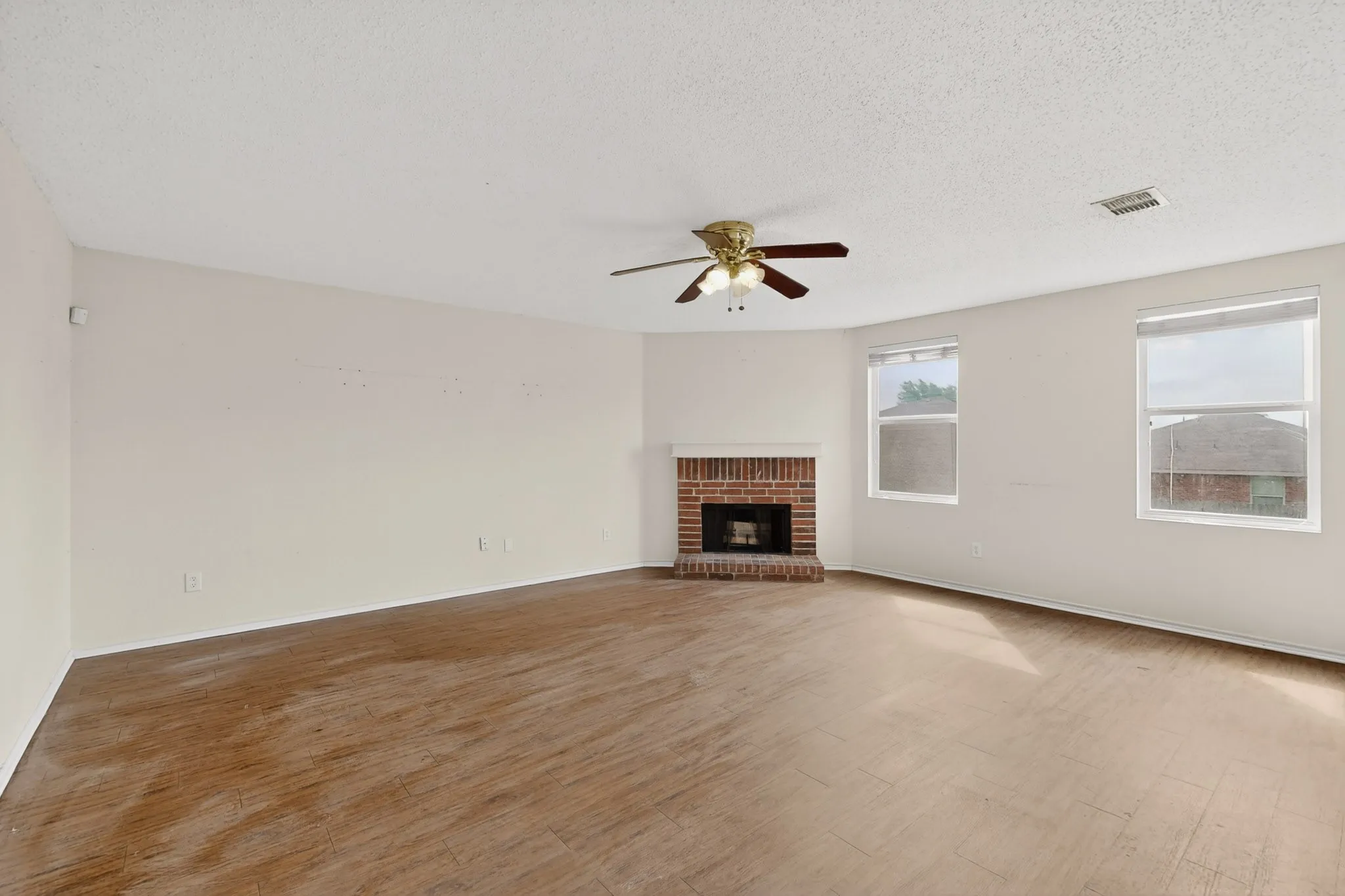 Unfurnished living room featuring light wood-type flooring, ceiling fan, a brick fireplace, and a textured ceiling