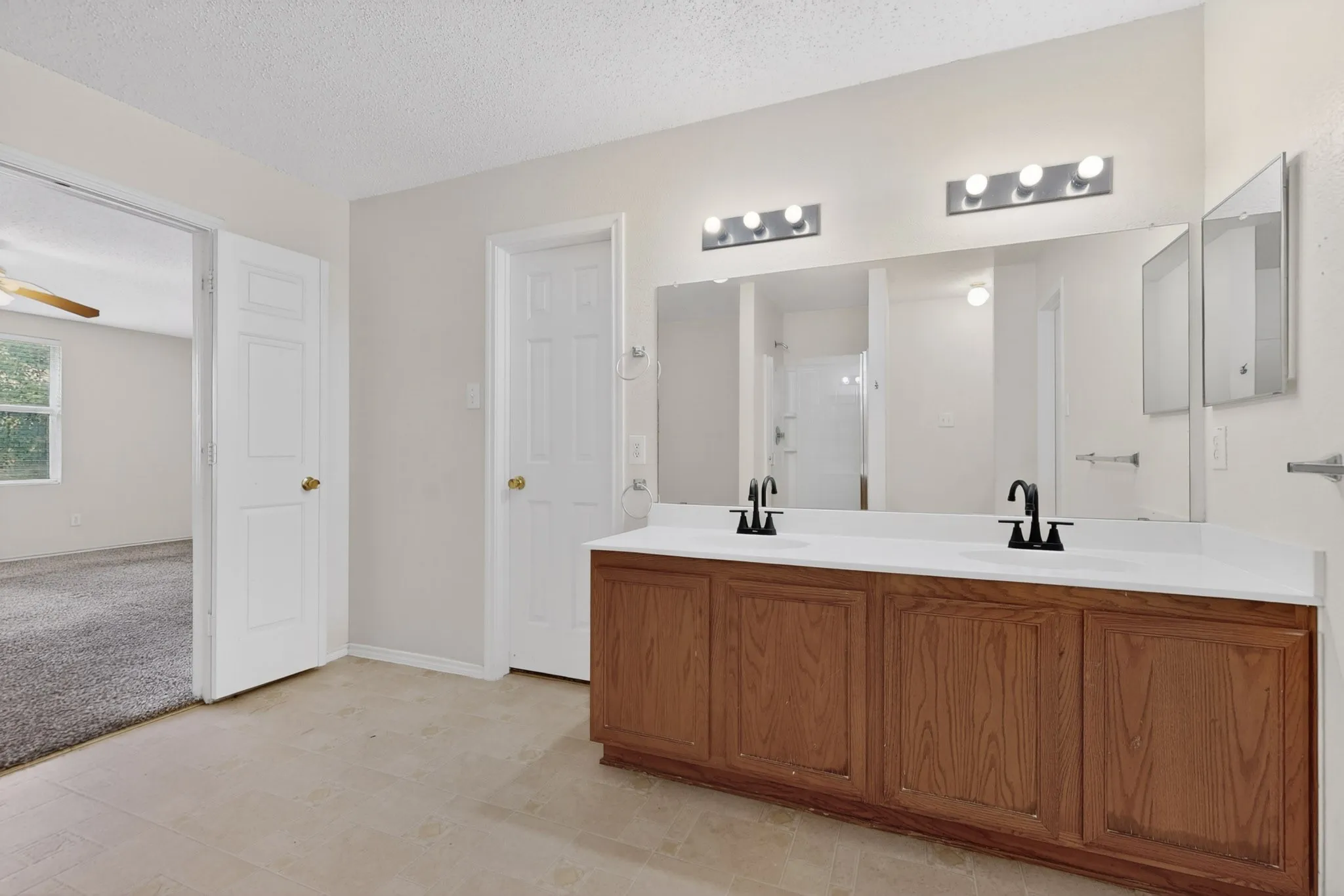 Full bathroom with double vanity, a textured ceiling, a shower stall, ceiling fan, and light colored carpet