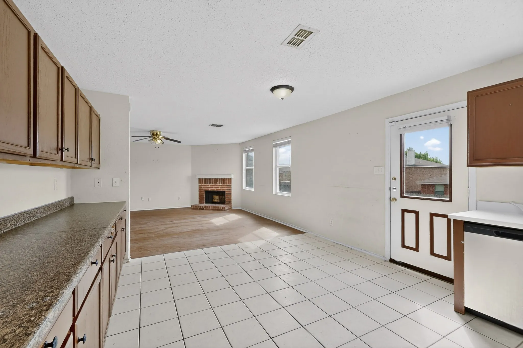 Unfurnished living room with a brick fireplace, a ceiling fan, healthy amount of natural light, and a textured ceiling
