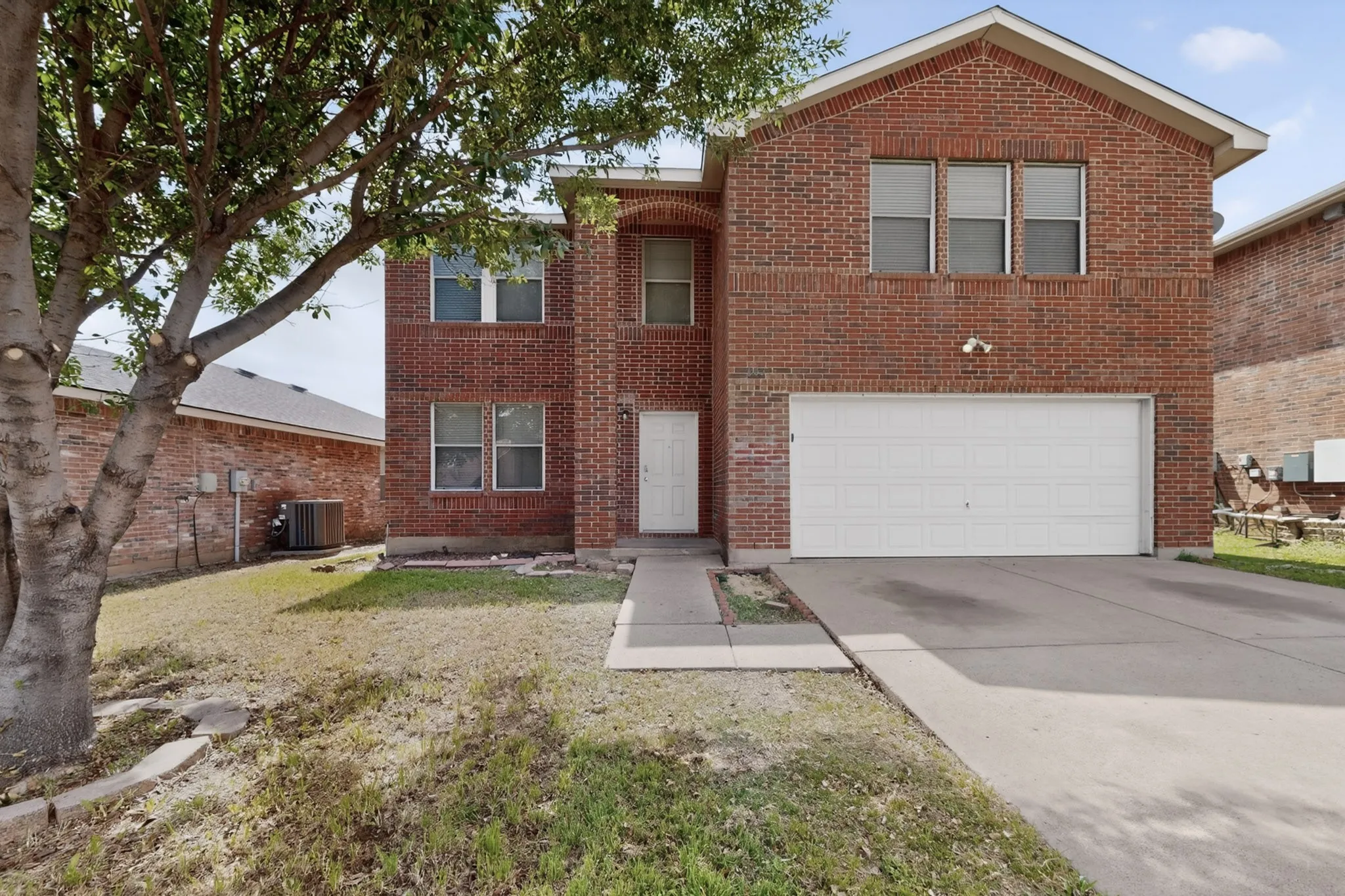 Traditional-style house featuring a front lawn, driveway, brick siding, and a garage