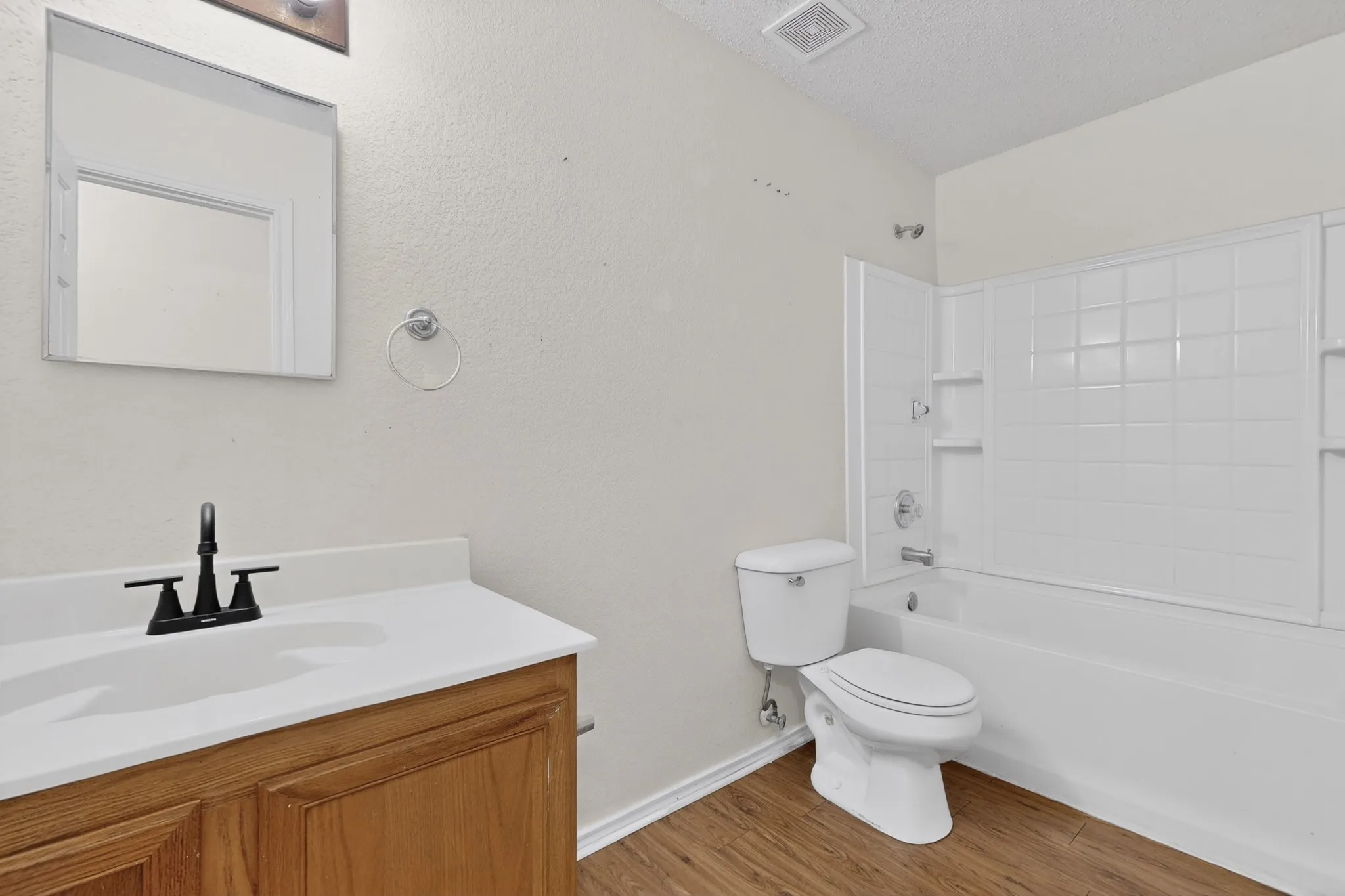 Bathroom featuring vanity, tub / shower combination, light wood-type flooring, and a textured ceiling