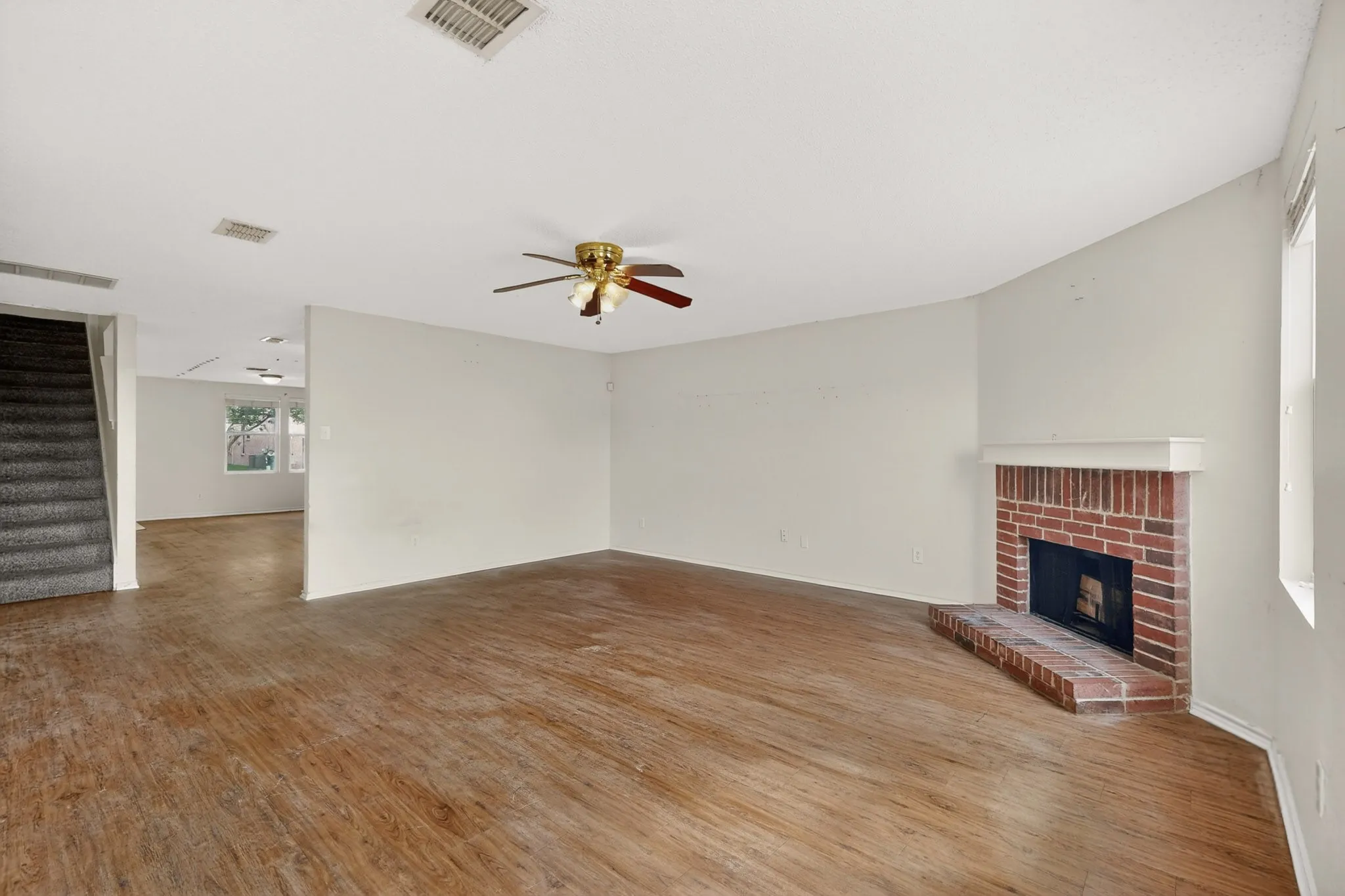 Unfurnished living room with wood finished floors, a ceiling fan, and a brick fireplace