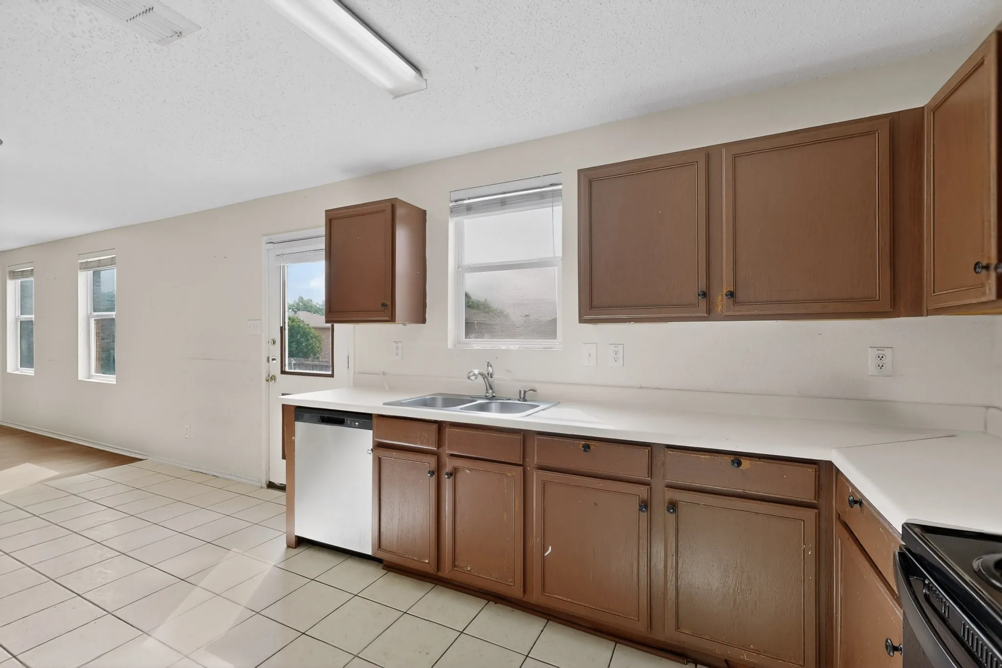 Kitchen with light countertops, stainless steel dishwasher, wood finish cabinetry, a textured ceiling, and black range with electric stovetop
