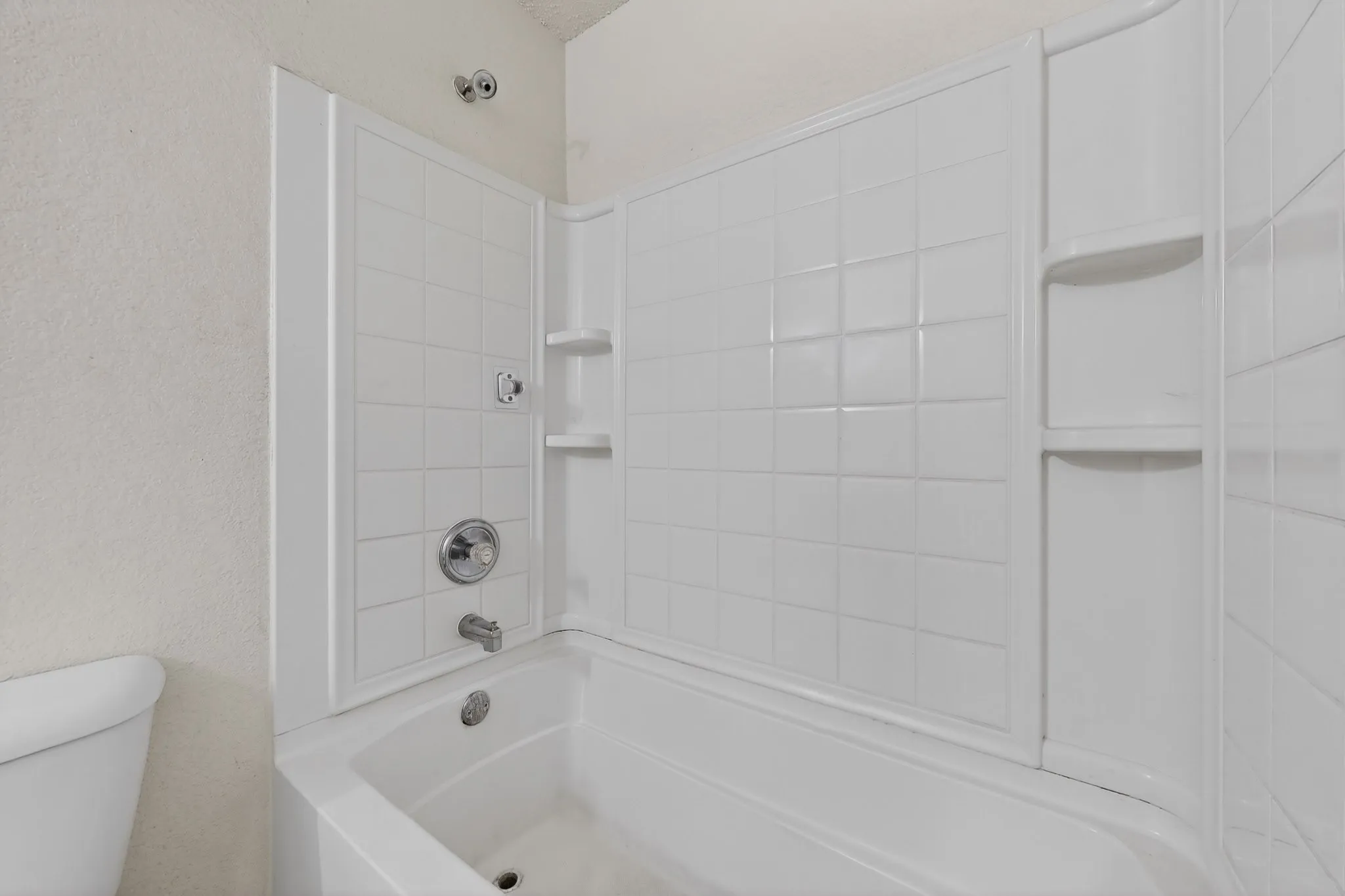 Full bathroom with a textured wall and bathtub / shower combination