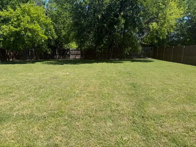 Expansive grassy yard featuring a wood privacy fence and mature trees providing natural shade