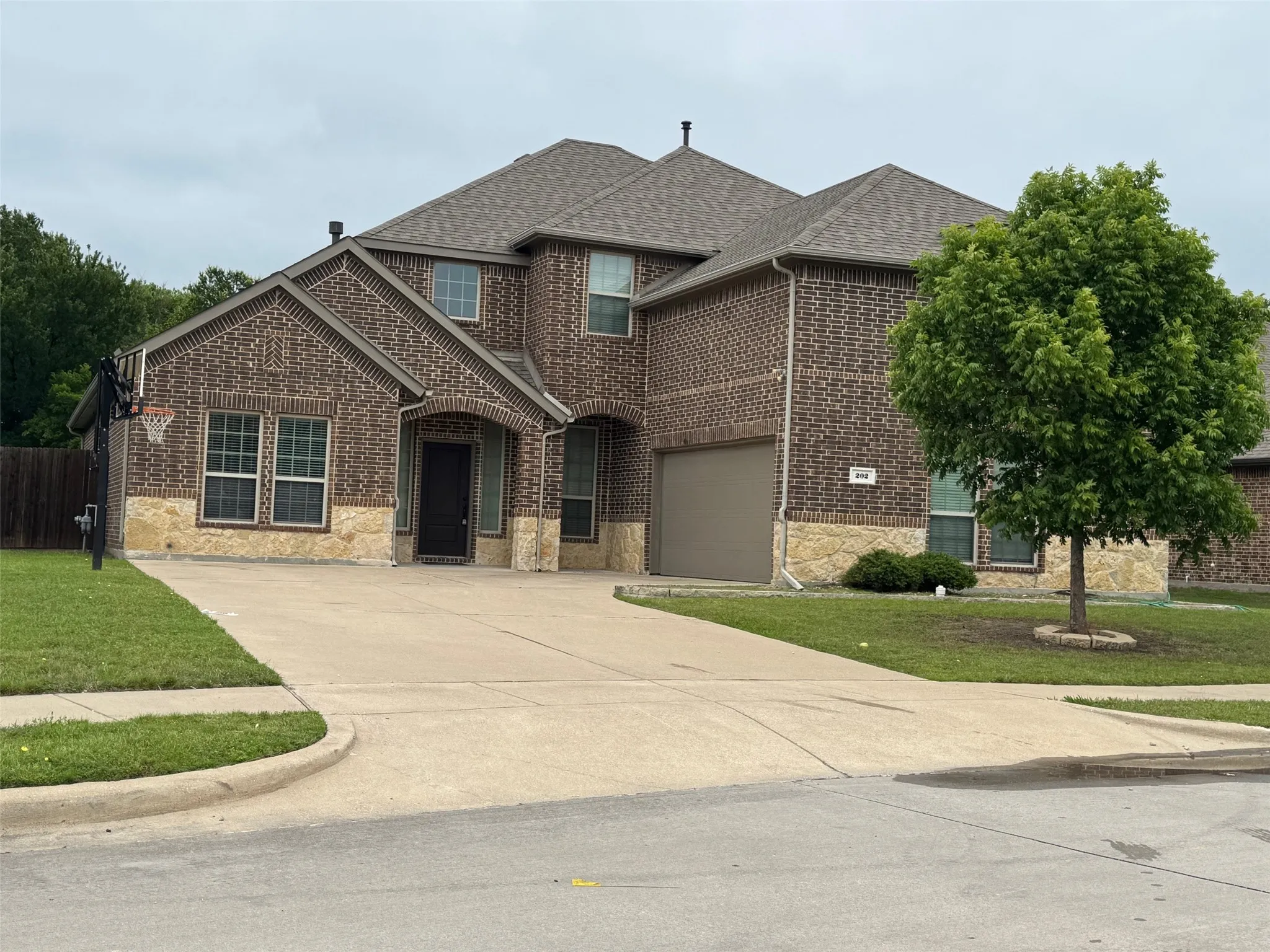 Two-story brick facade residence featuring a two-car garage, an arched entryway, stone detailing, and a shingle roof