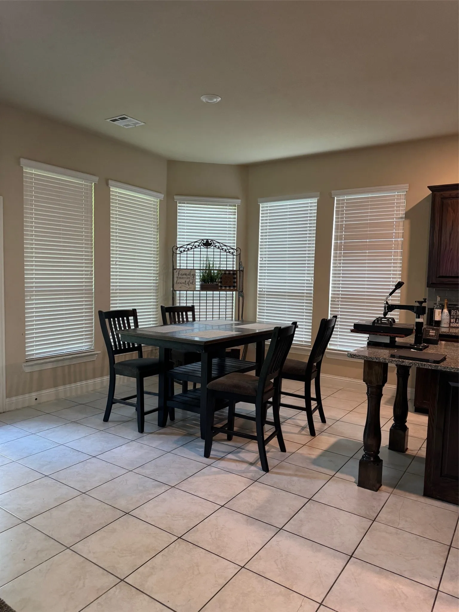 Bay window dining area featuring tile flooring, multiple windows with blinds, a recessed ceiling light, and built-in cabinetry with a stone-finish countertop