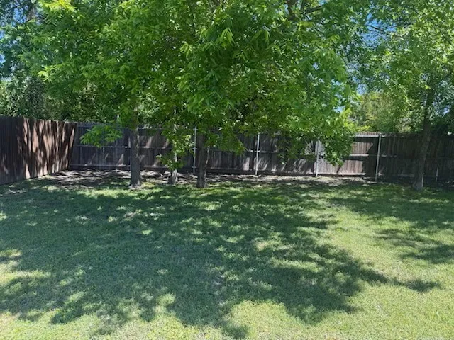 Expansive backyard featuring a lush lawn, mature trees providing natural shade, and a privacy fence enclosing the perimeter