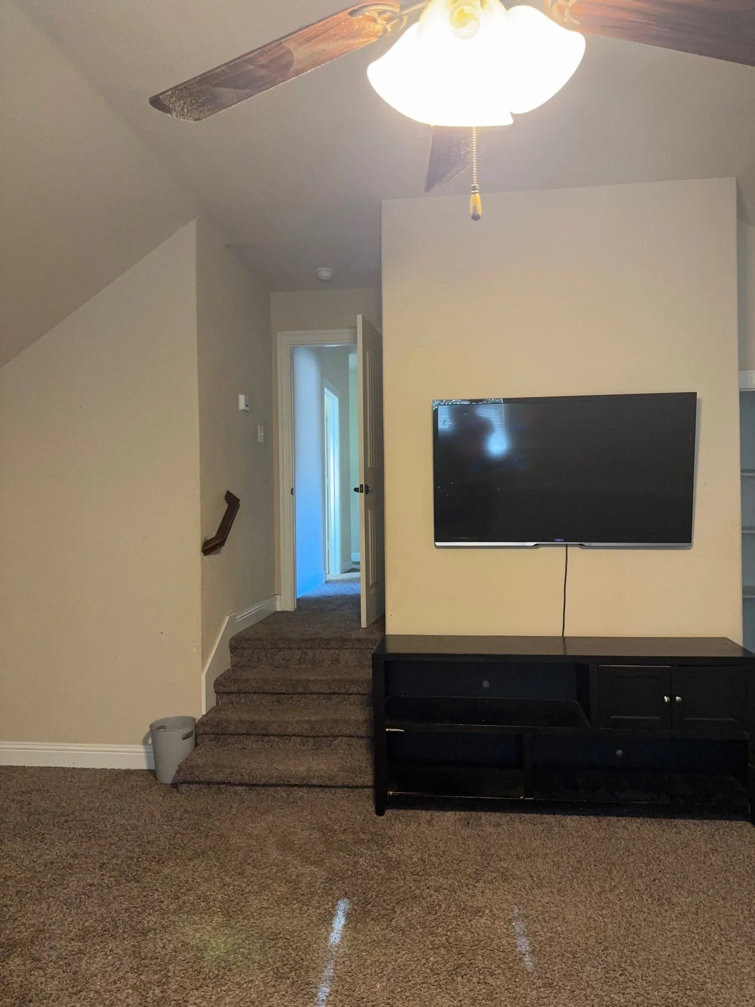 Carpeted room featuring a ceiling fan with light fixture, built-in shelving, and neutral wall tones