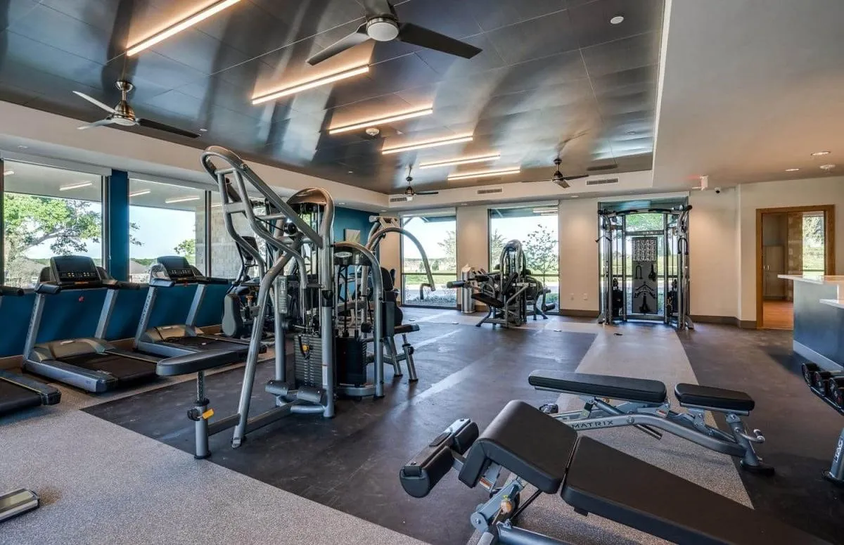 Fitness center featuring extensive exercise equipment, large windows providing natural light, ceiling fans, and overhead strip lighting