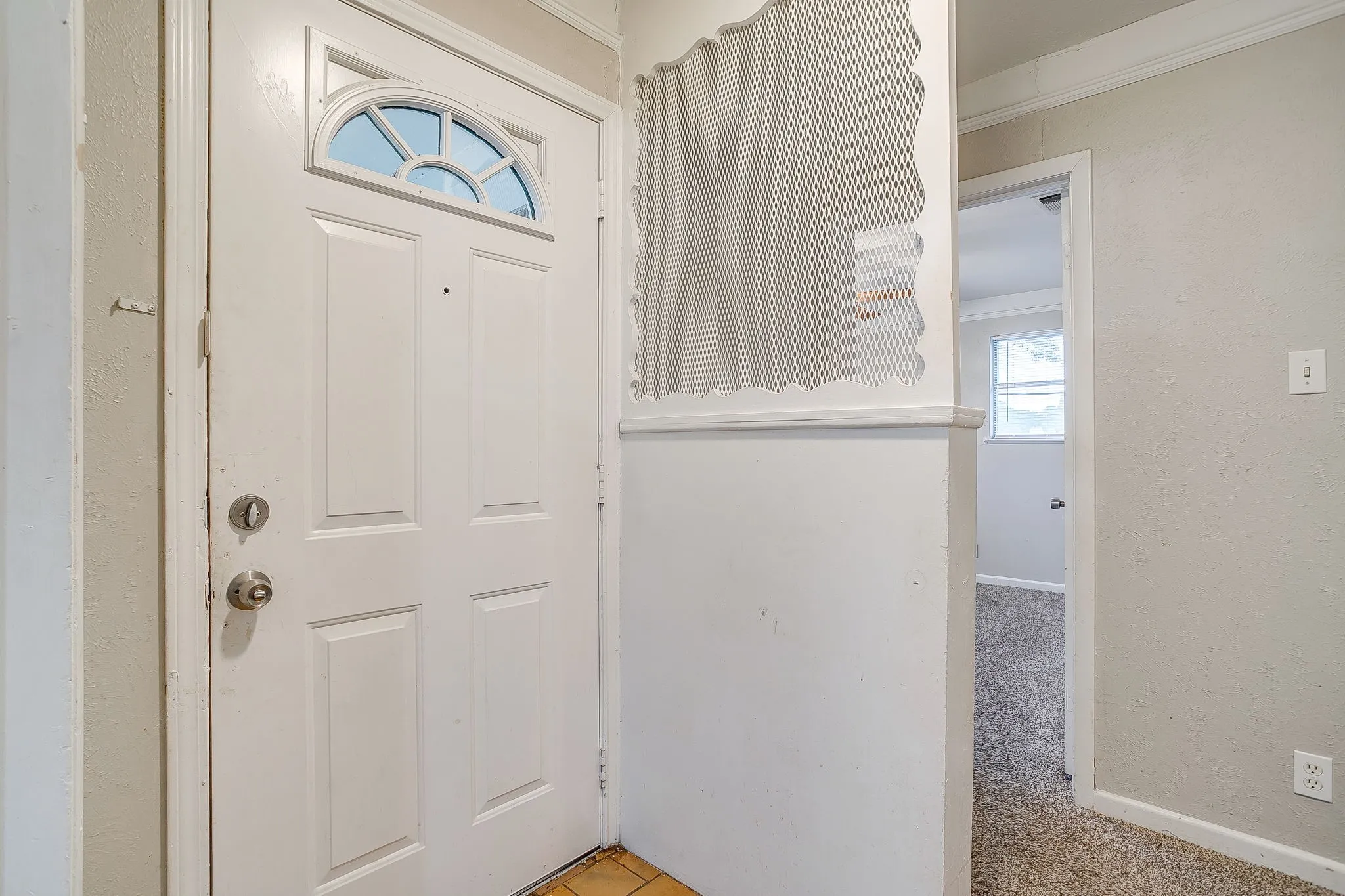 White paneled entry door with an arched transom window, featuring a metal screen partition