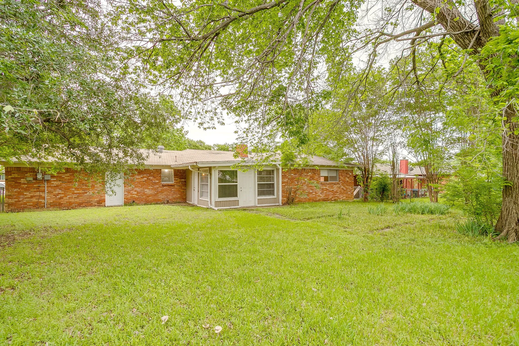 Expansive green lawn surrounds the rear of the property, featuring a red brick exterior, a screened-in porch with white framing, and mature trees providing natural canopy