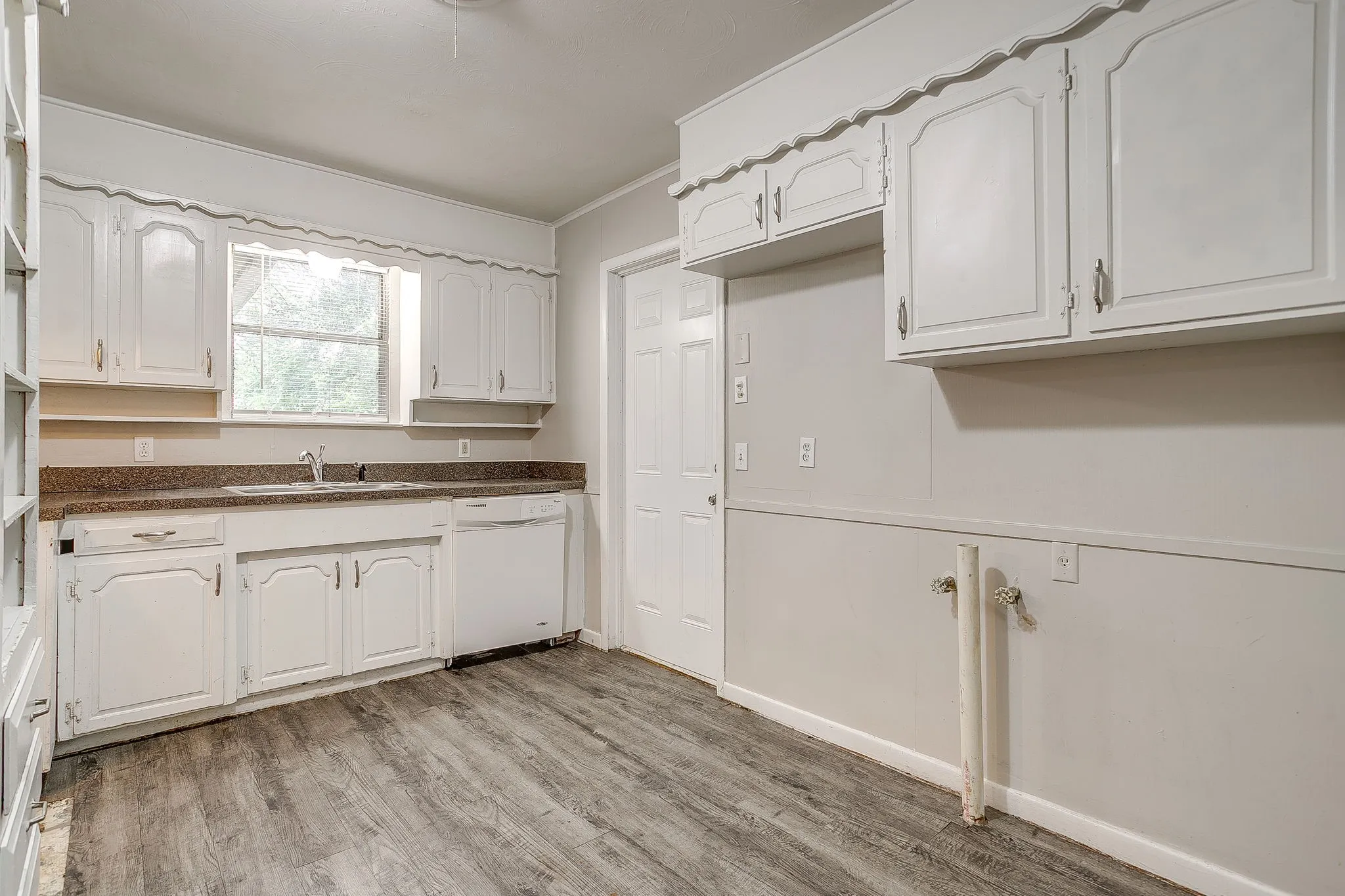 Kitchen featuring wood-finish flooring, white cabinetry, a single-basin sink, a built-in dishwasher, and a window