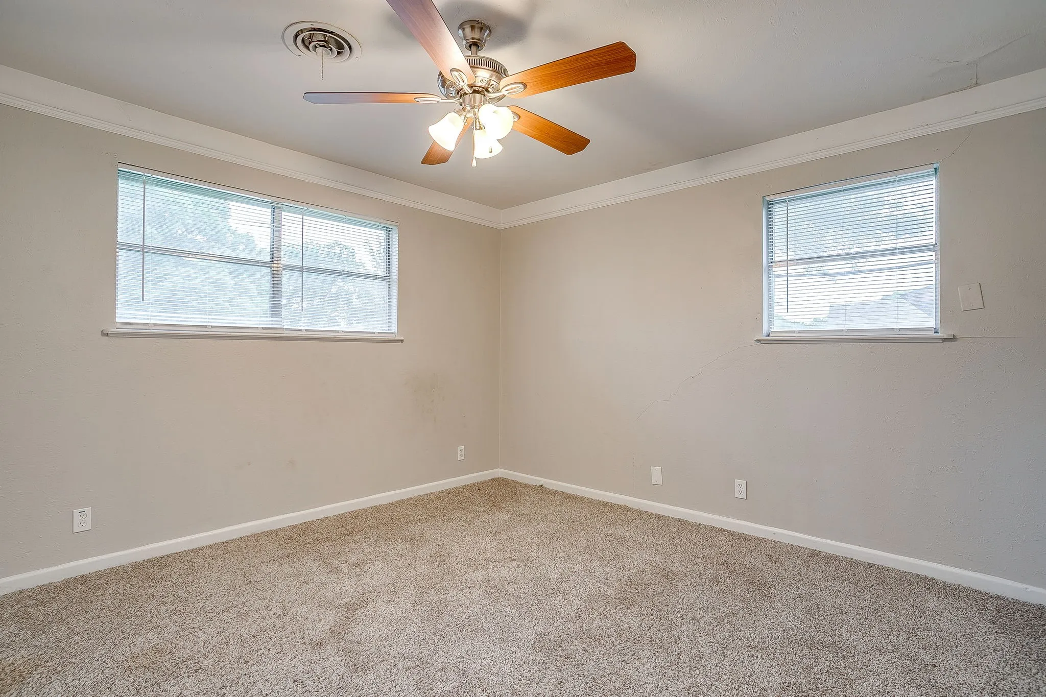 Carpeted interior space featuring two windows with horizontal blinds, a ceiling fan with integrated lighting, and crown molding