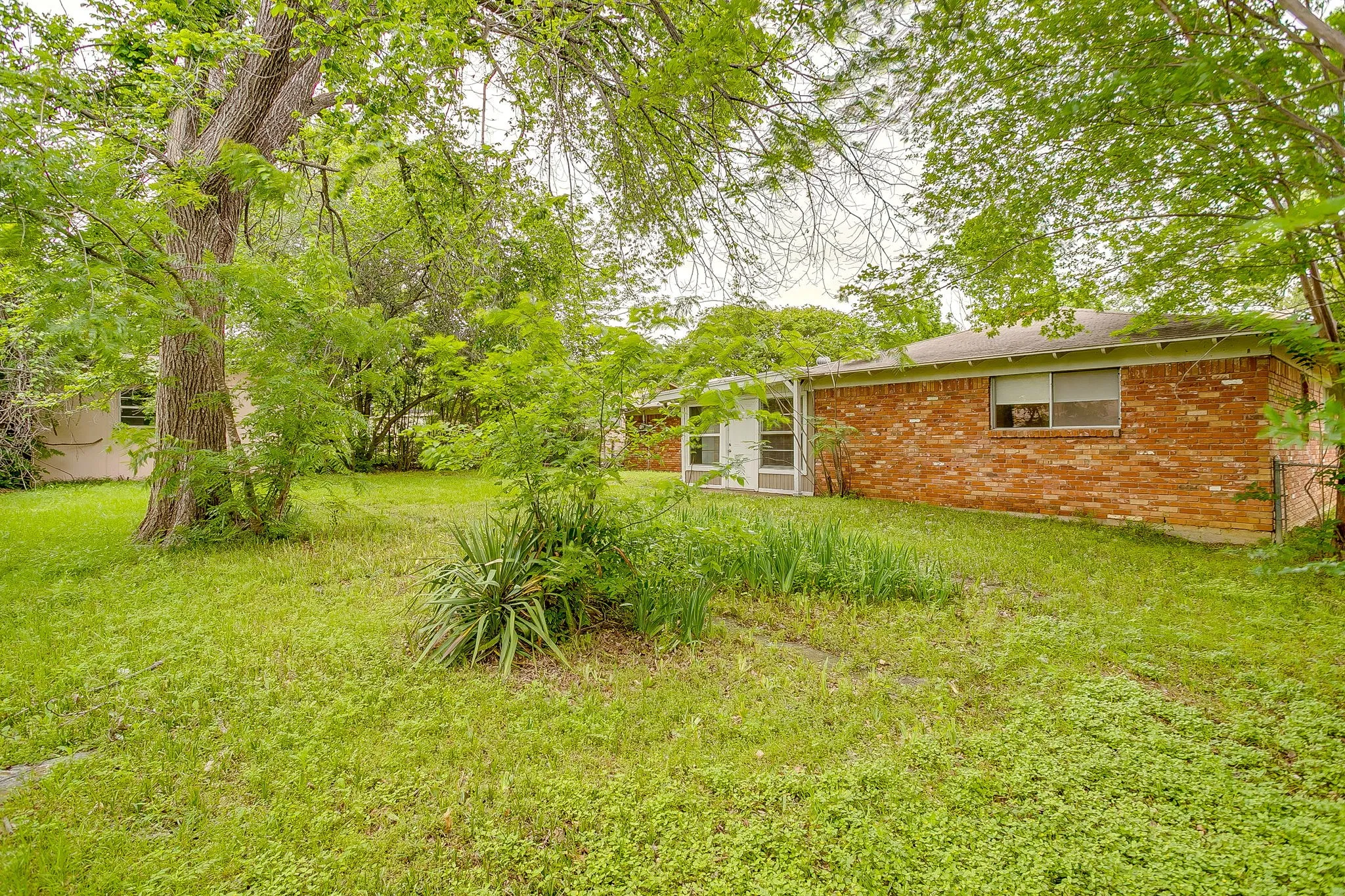 Spacious backyard featuring mature trees, established shrubs, and a brick exterior