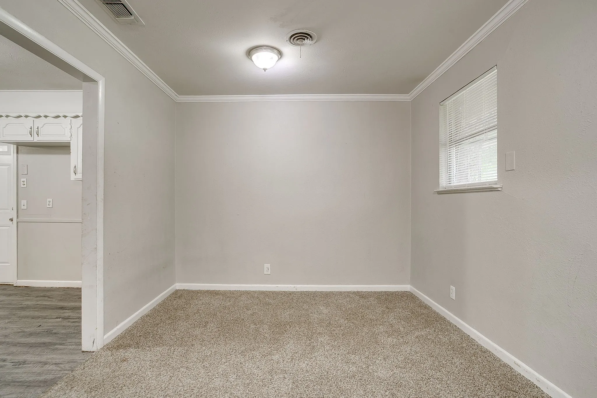 Carpeted room featuring a single window with blinds, overhead lighting, crown molding, and a neutral wall finish