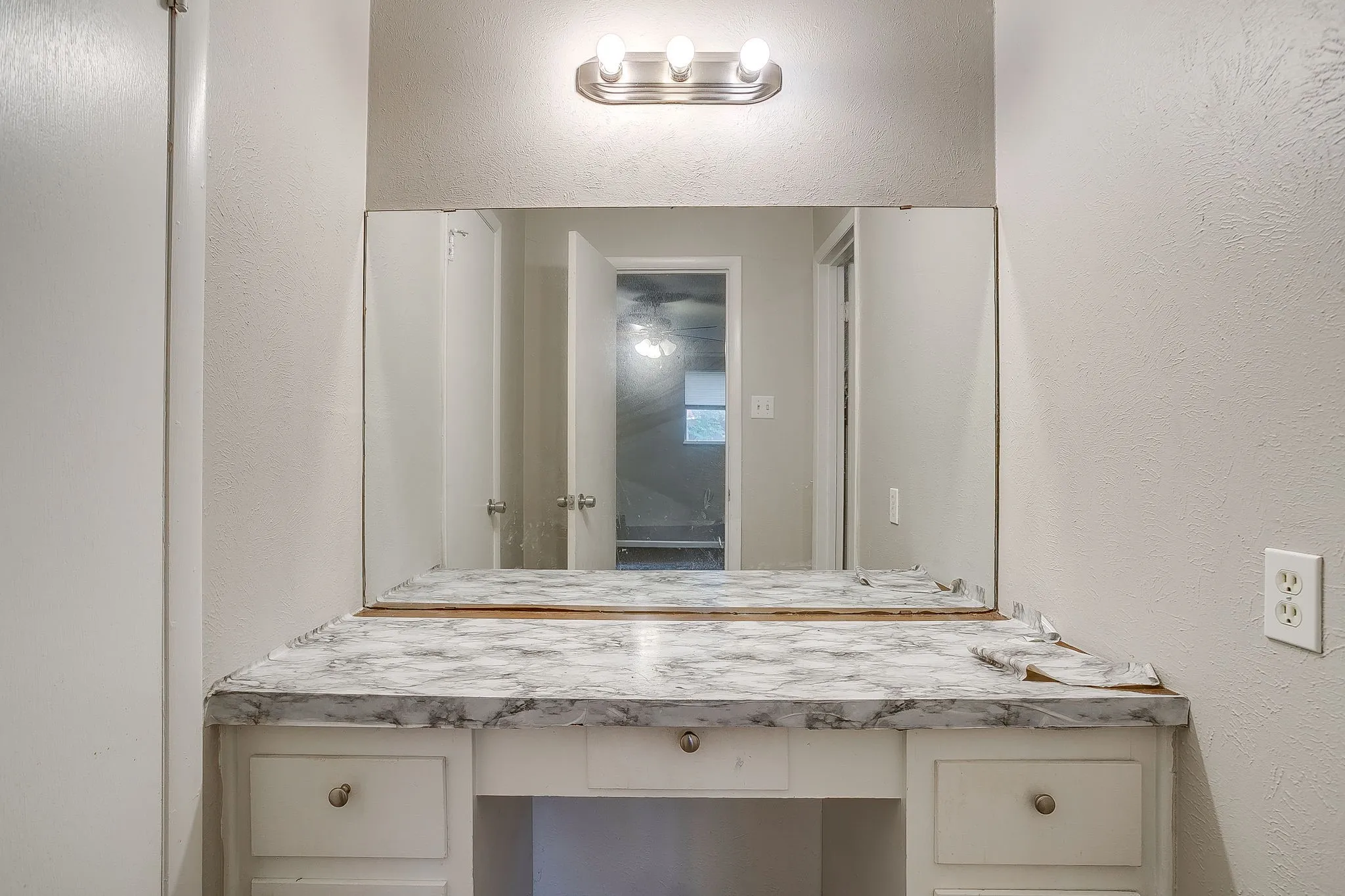 Vanity area featuring a built-in countertop with a faux stone finish, integrated mirror, and a three-light fixture