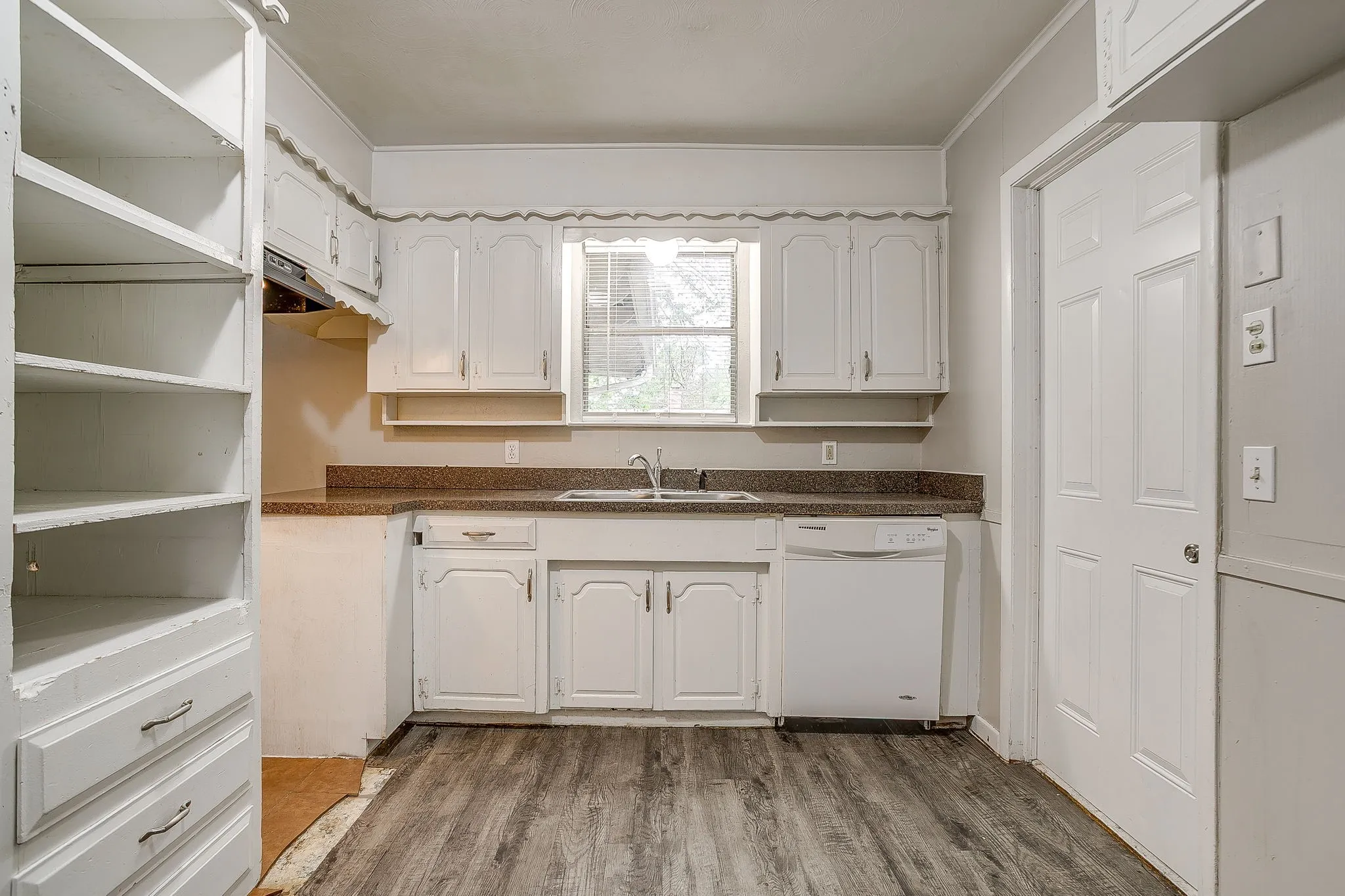 Kitchen featuring wood-finish flooring, white cabinetry, a built-in dishwasher, and a window above the sink