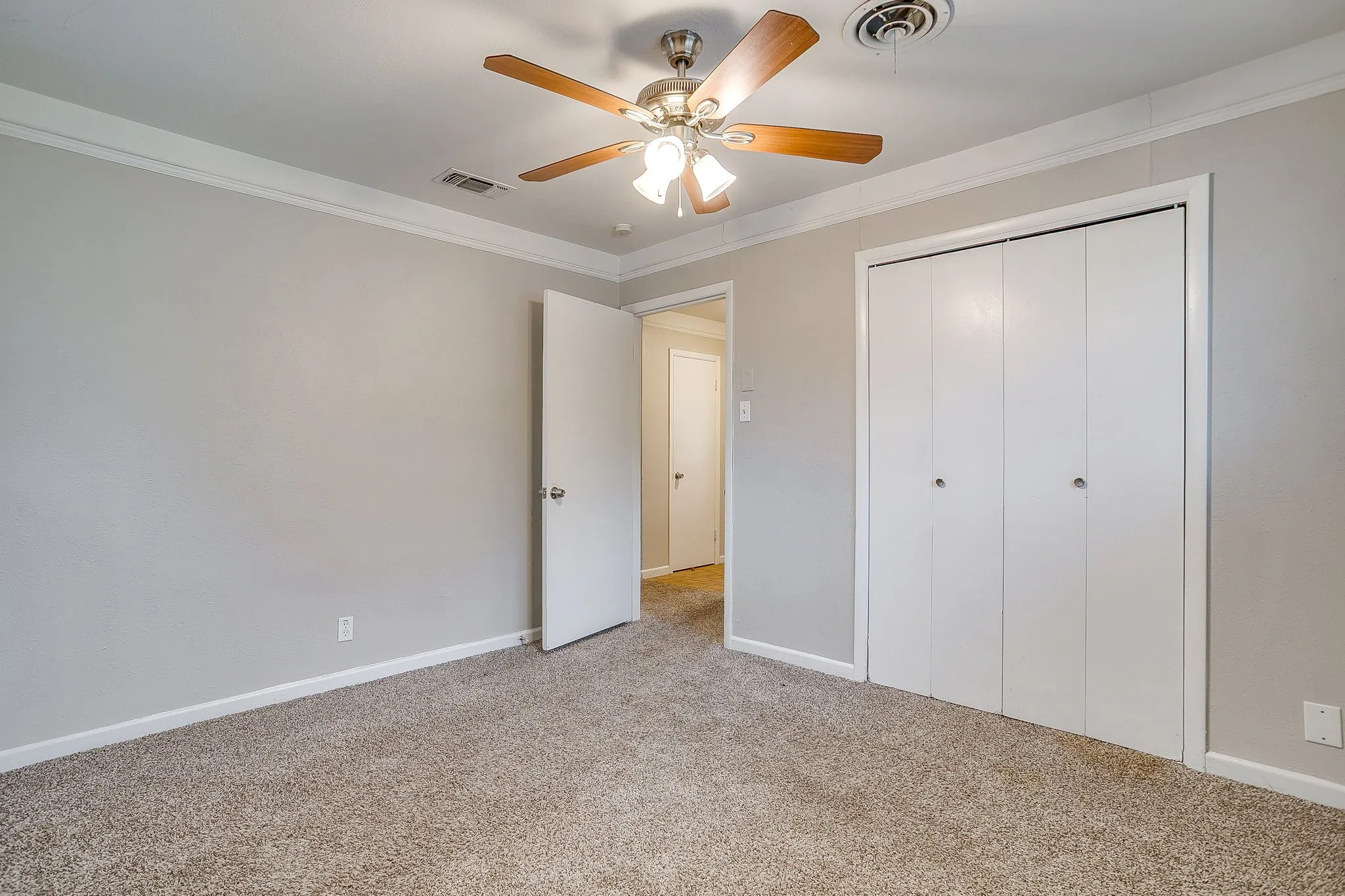 Carpeted room featuring a double bifold closet, a ceiling fan with light fixture, light gray wall paint, white crown molding, and white baseboards