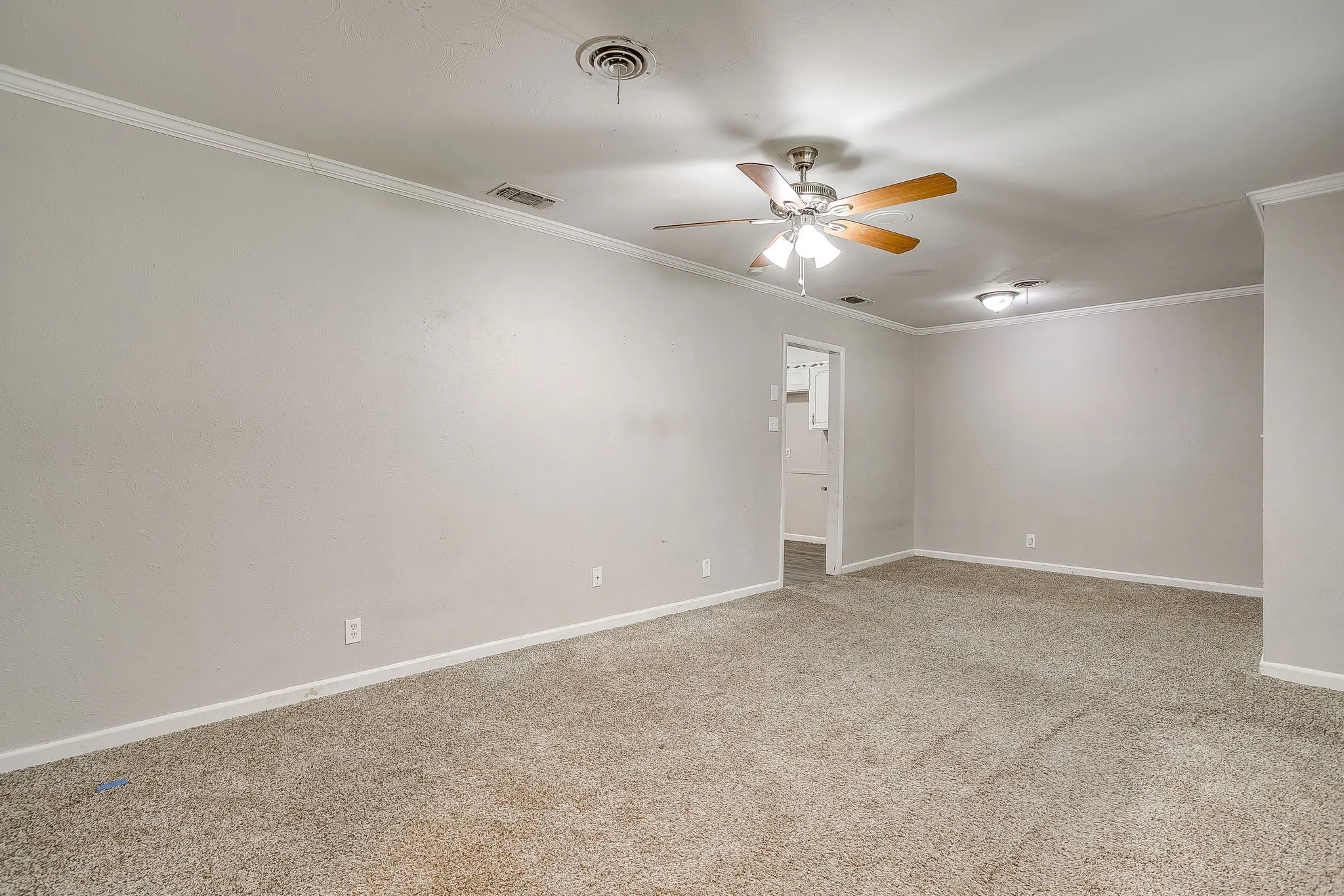 Spacious room featuring neutral carpeting, light-toned walls, and white crown molding