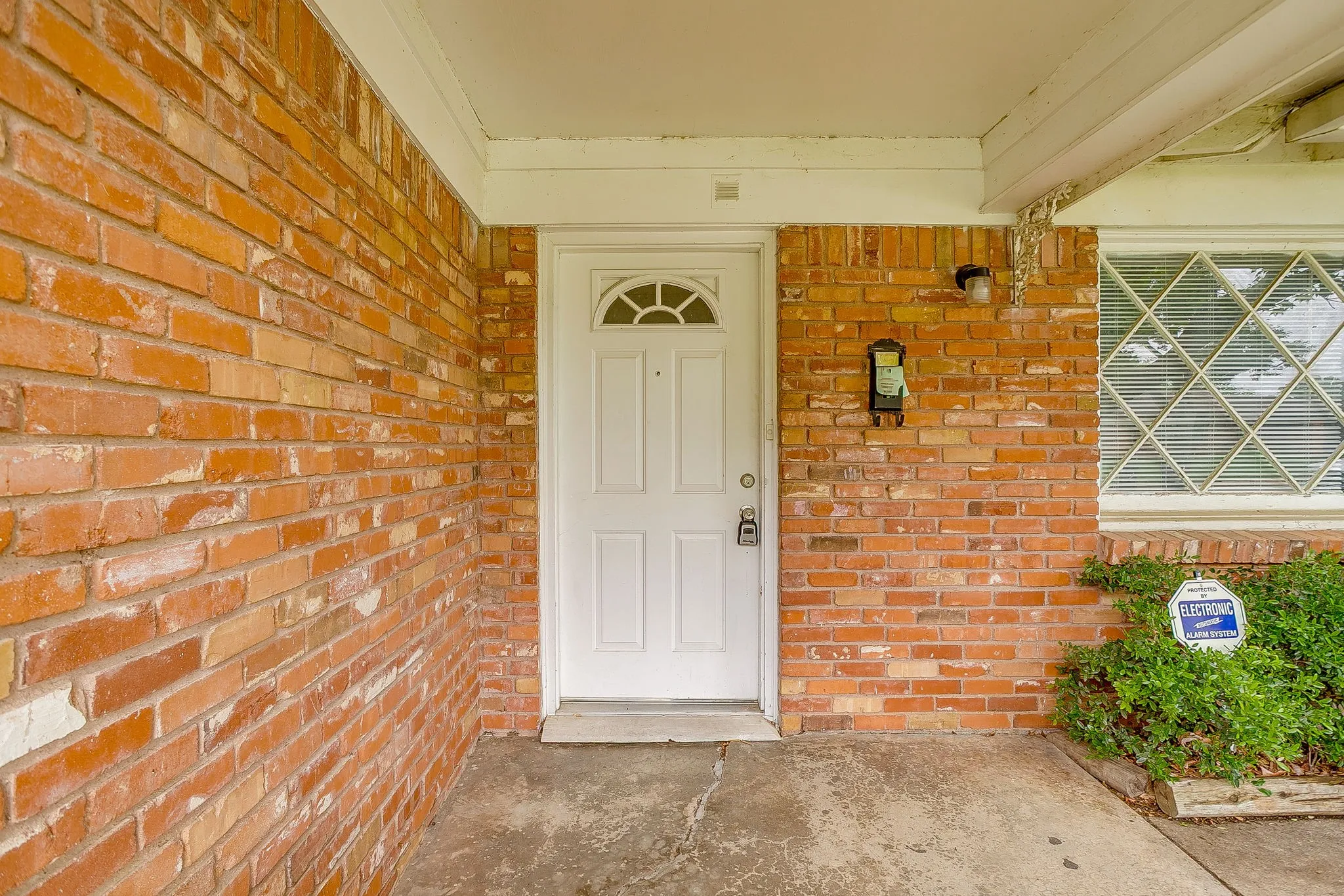 Brick exterior featuring a white entry door with an arched window, a covered porch, a wall-mounted light fixture, and a window with decorative muntins