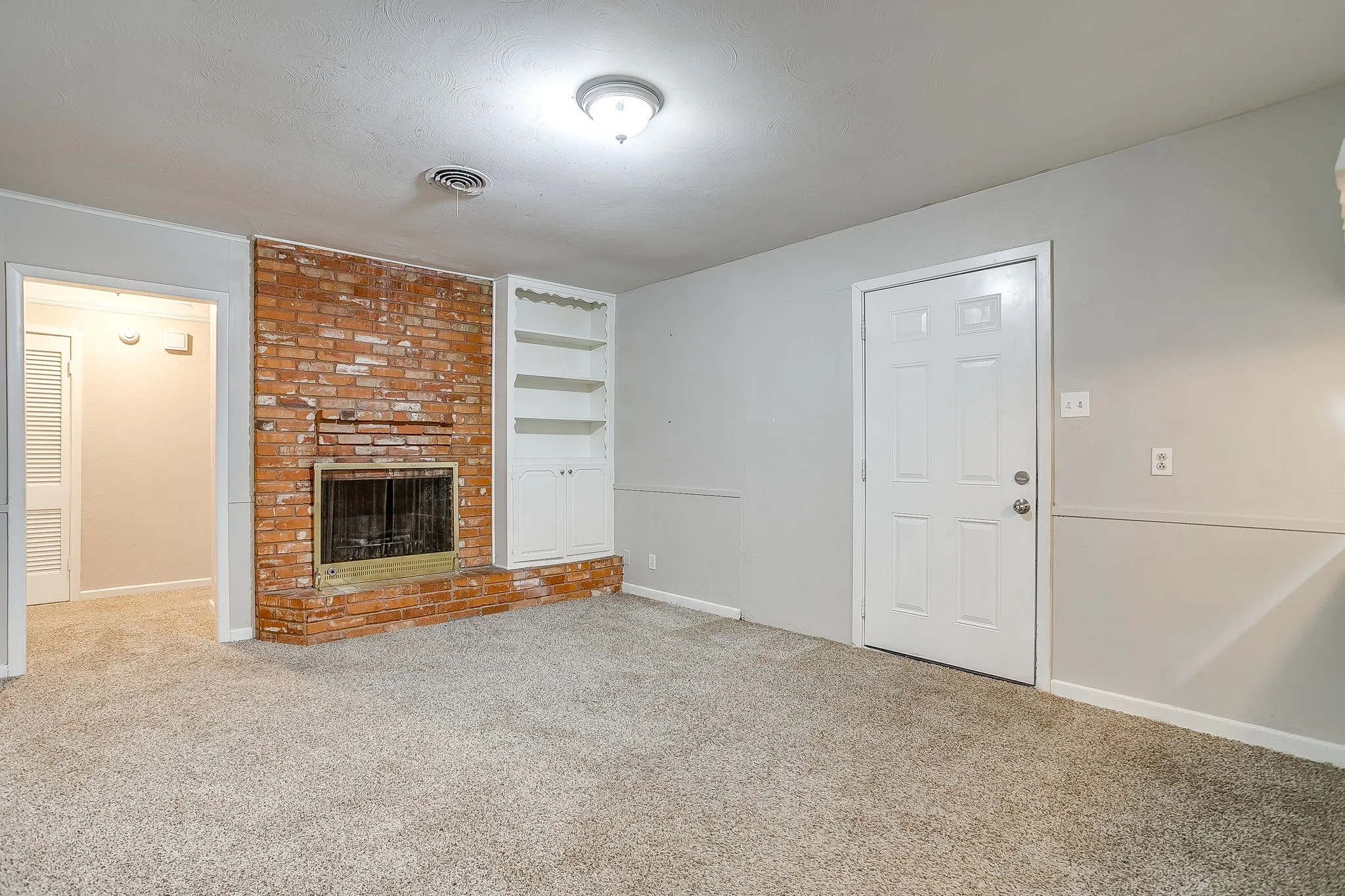 Spacious interior room featuring a brick fireplace, built-in shelving, light gray wall paint, and neutral carpeting