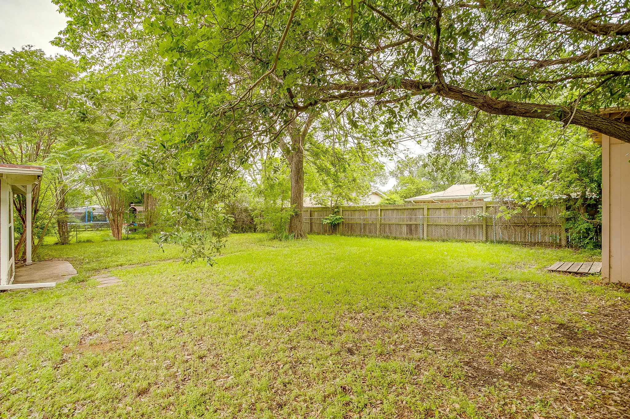 Expansive backyard featuring a lush lawn, mature trees, wood privacy fencing, and a concrete patio