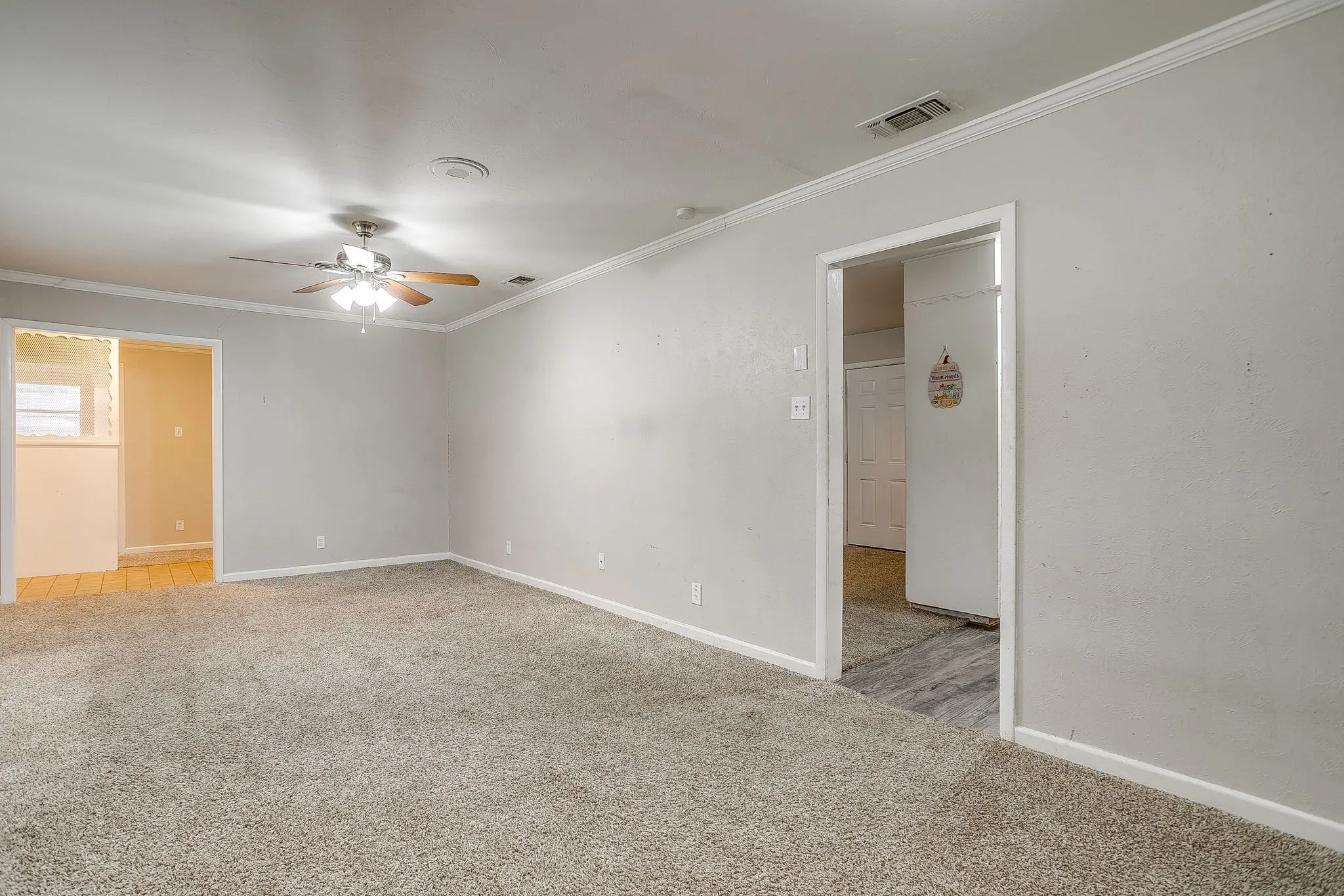 Spacious room featuring neutral carpeting, light gray wall tones, crown molding, and a ceiling fan with light fixture