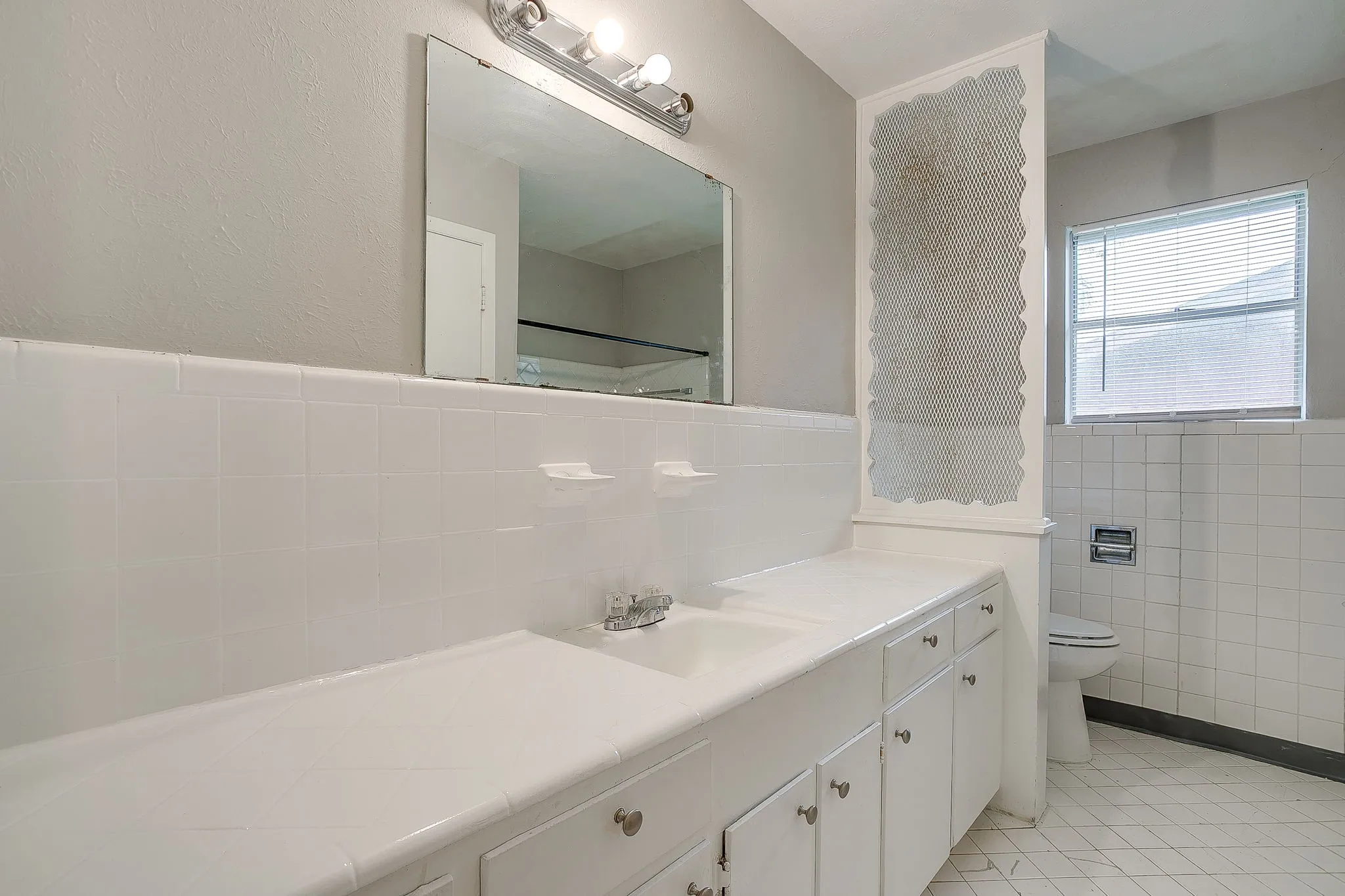 Double vanity with integrated sinks, white tile backsplash, and white cabinetry