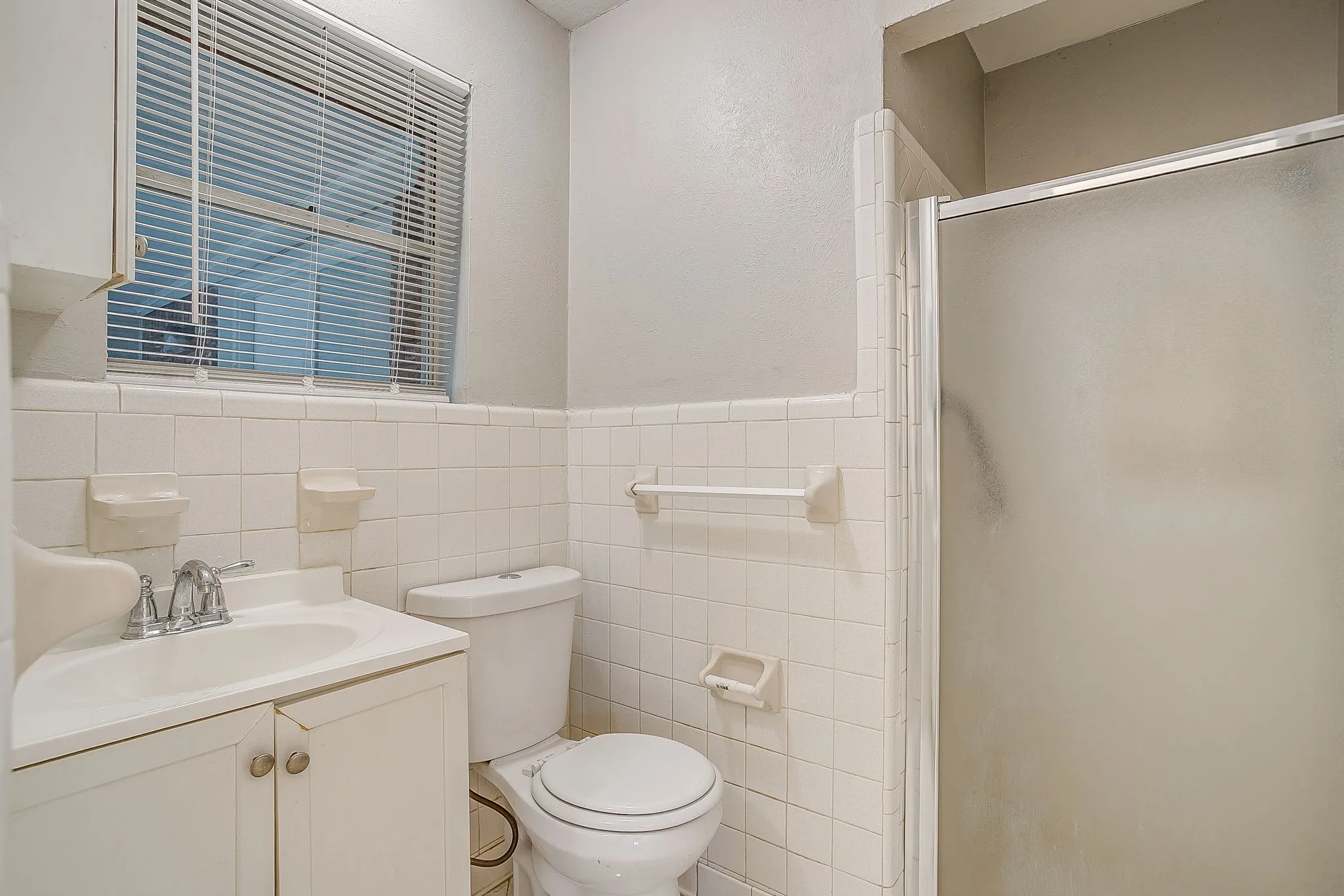 Bathroom featuring white wall tile, a single vanity with storage, and a shower with a frosted glass enclosure