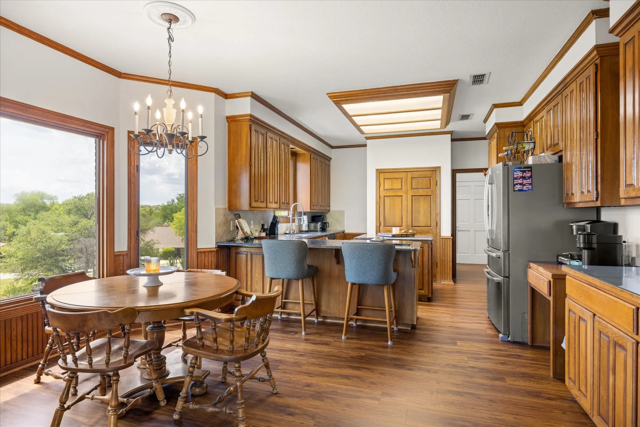 Dining area featuring dark wood-style floors, crown molding, a chandelier, and a wainscoted wall
