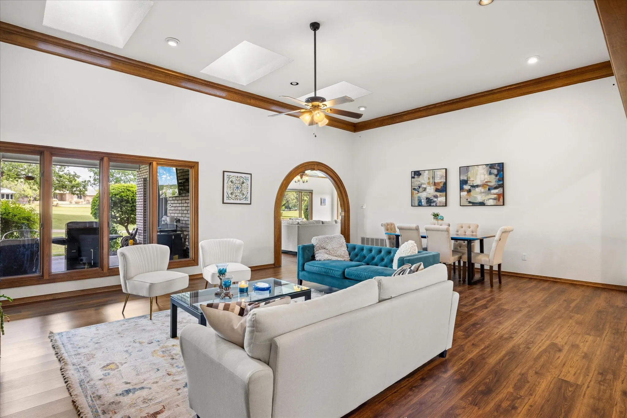 Living room featuring crown molding, wood finished floors, a ceiling fan, arched walkways, and a skylight