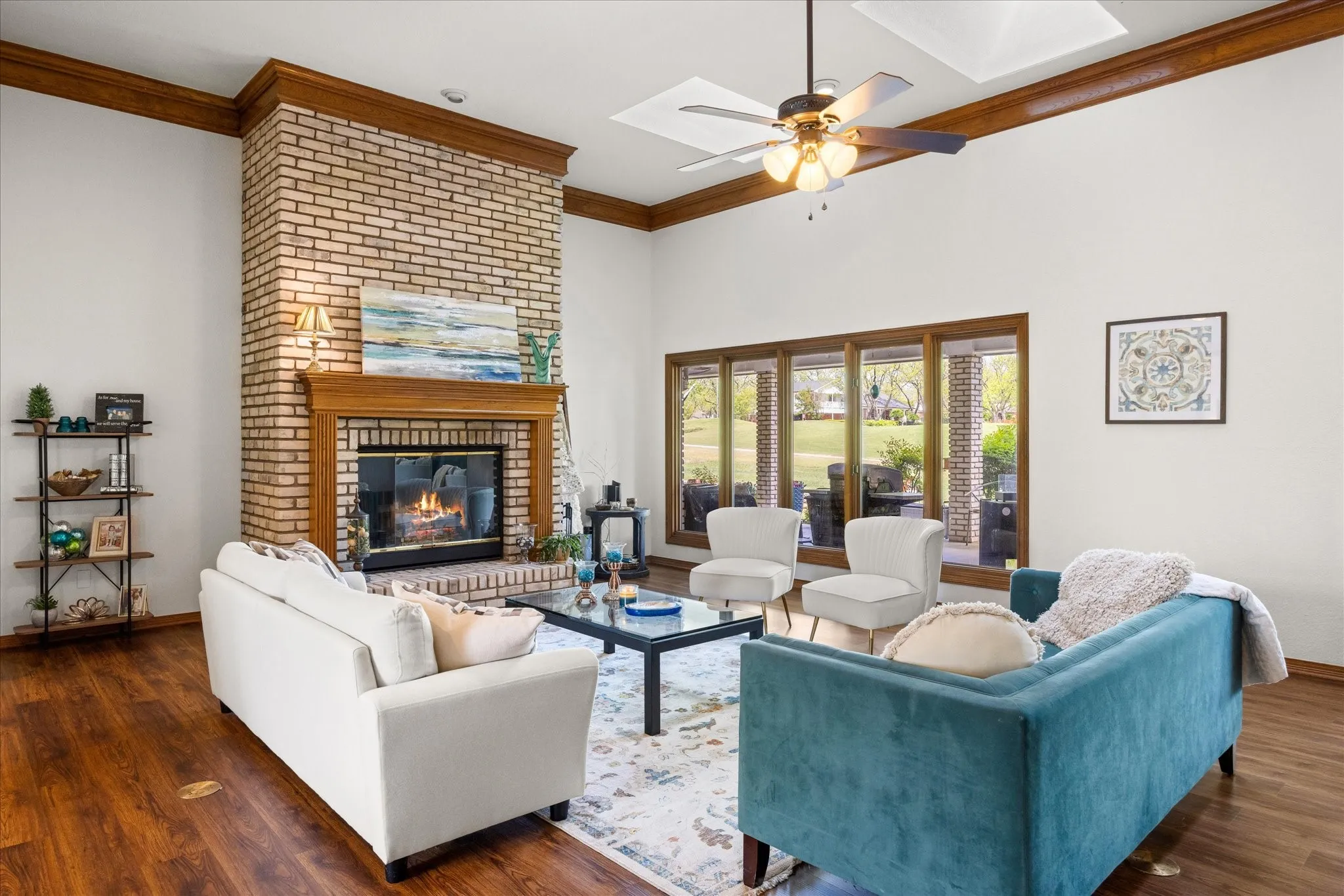 Living area with crown molding, dark wood-style flooring, ceiling fan, and a brick fireplace