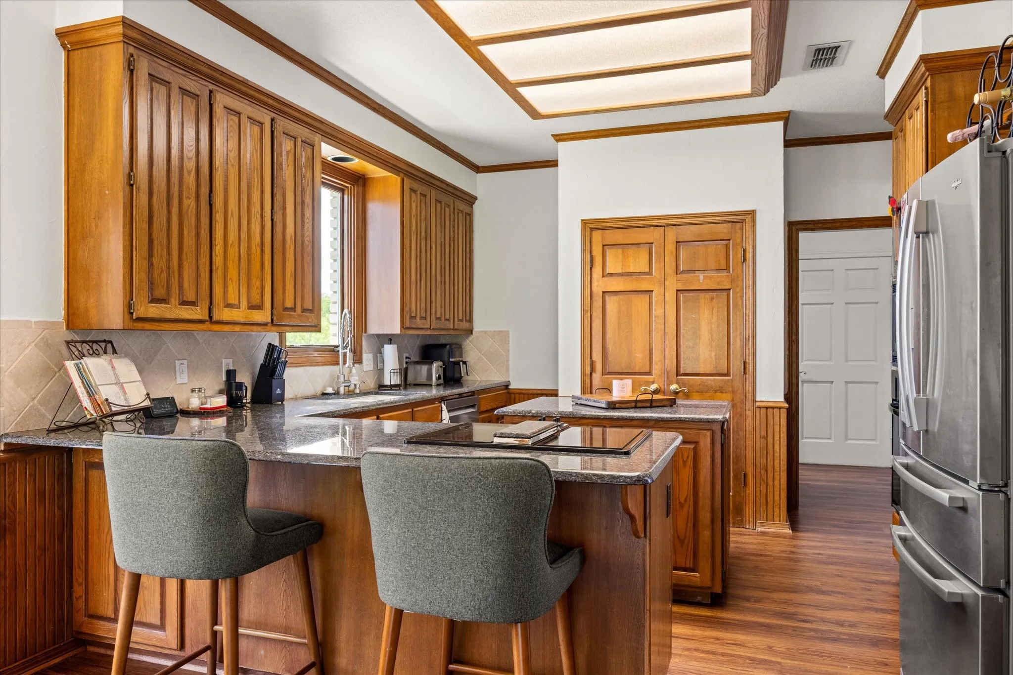 Kitchen featuring wood finish cabinets, crown molding, freestanding refrigerator, a peninsula, and dark stone counters