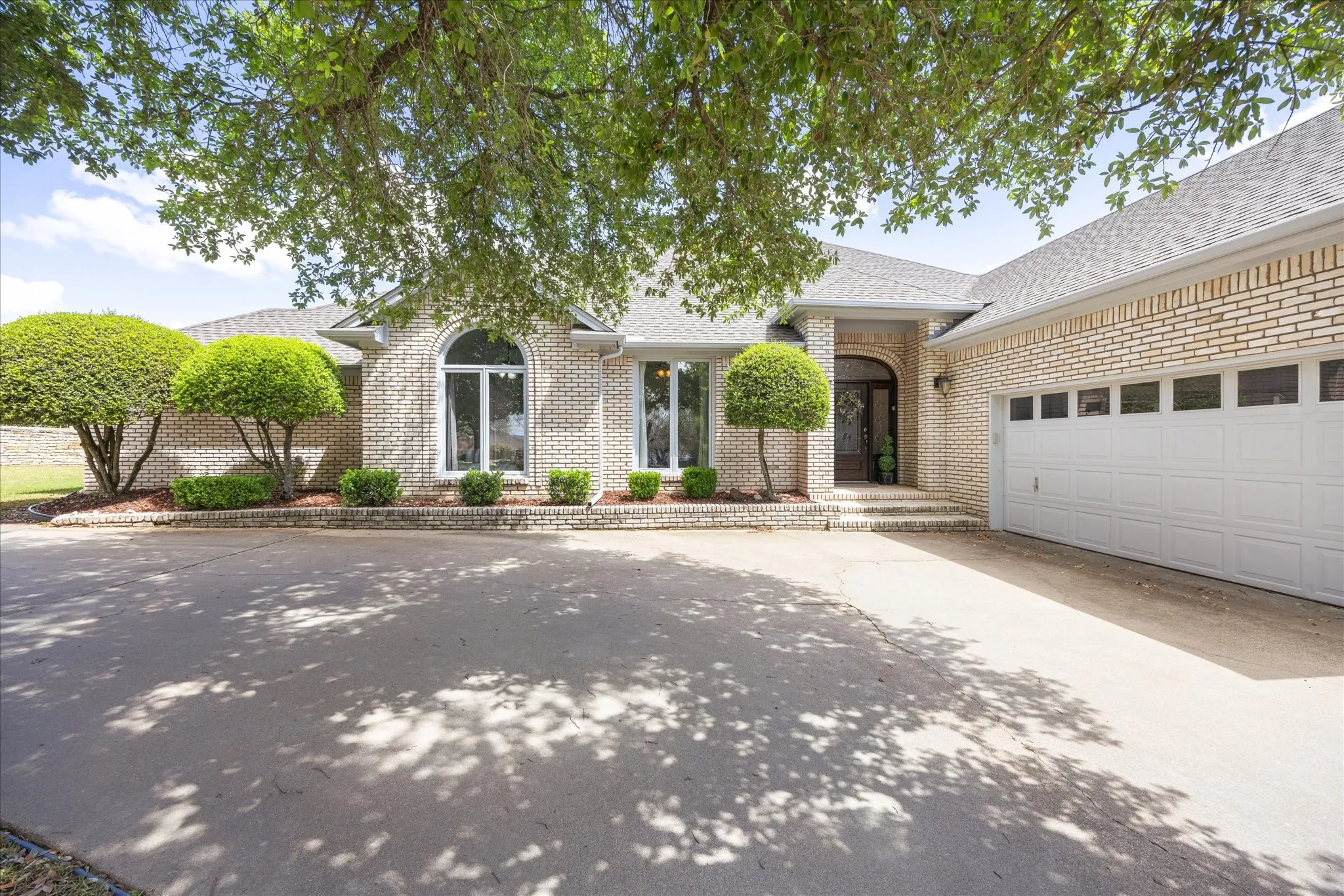 View of front of home with roof with shingles, concrete driveway, a garage, and brick siding