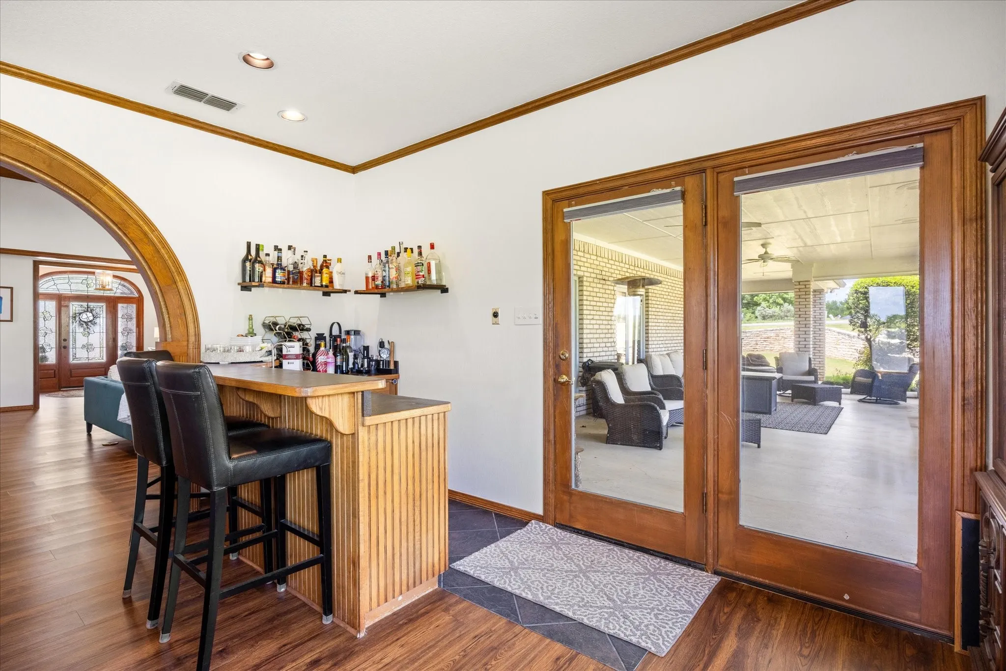 Indoor dry bar featuring arched walkways, dark wood finished floors, ornamental molding, recessed lighting, and french doors