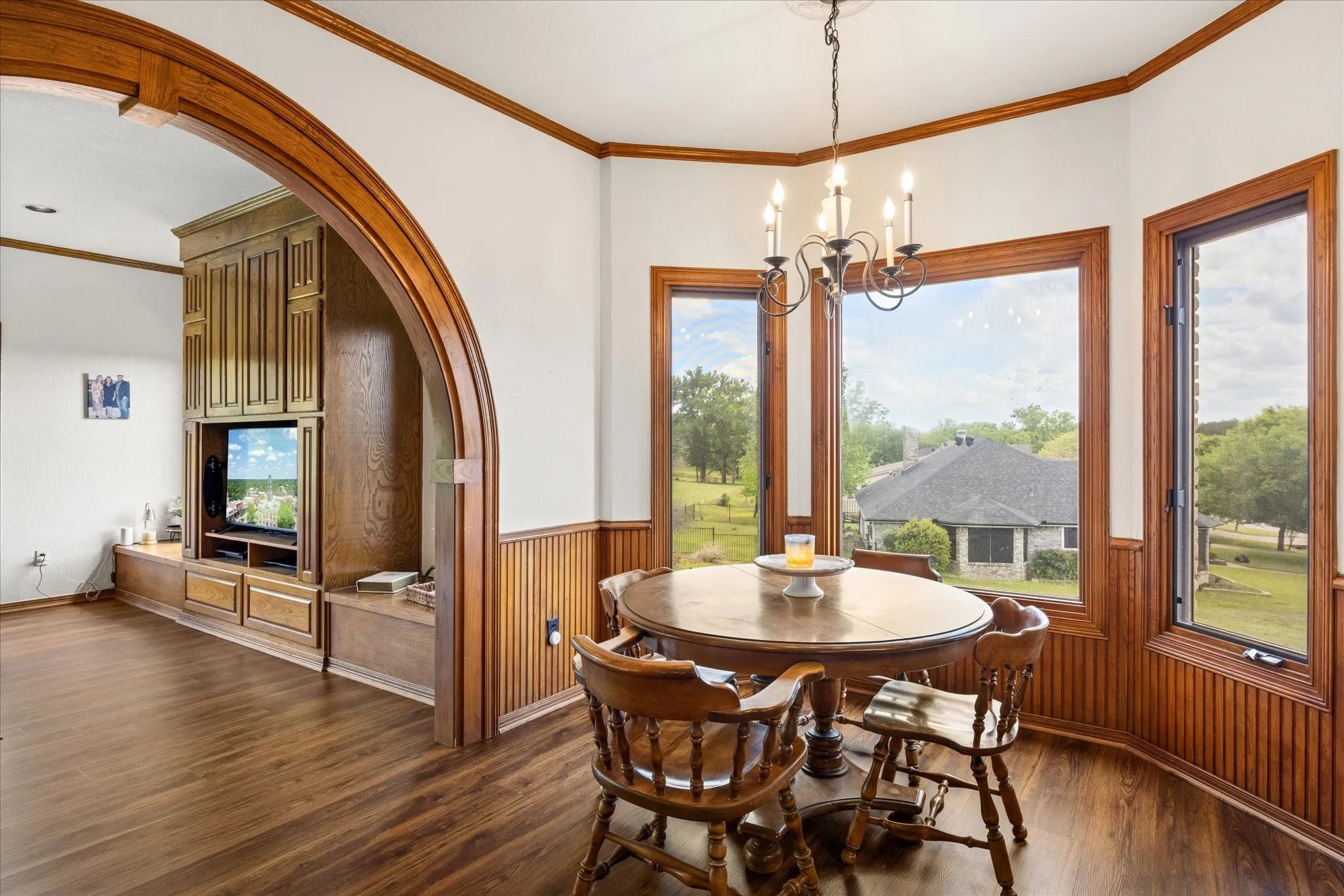 Dining space featuring arched walkways, crown molding, a chandelier, dark wood-type flooring, and wainscoting