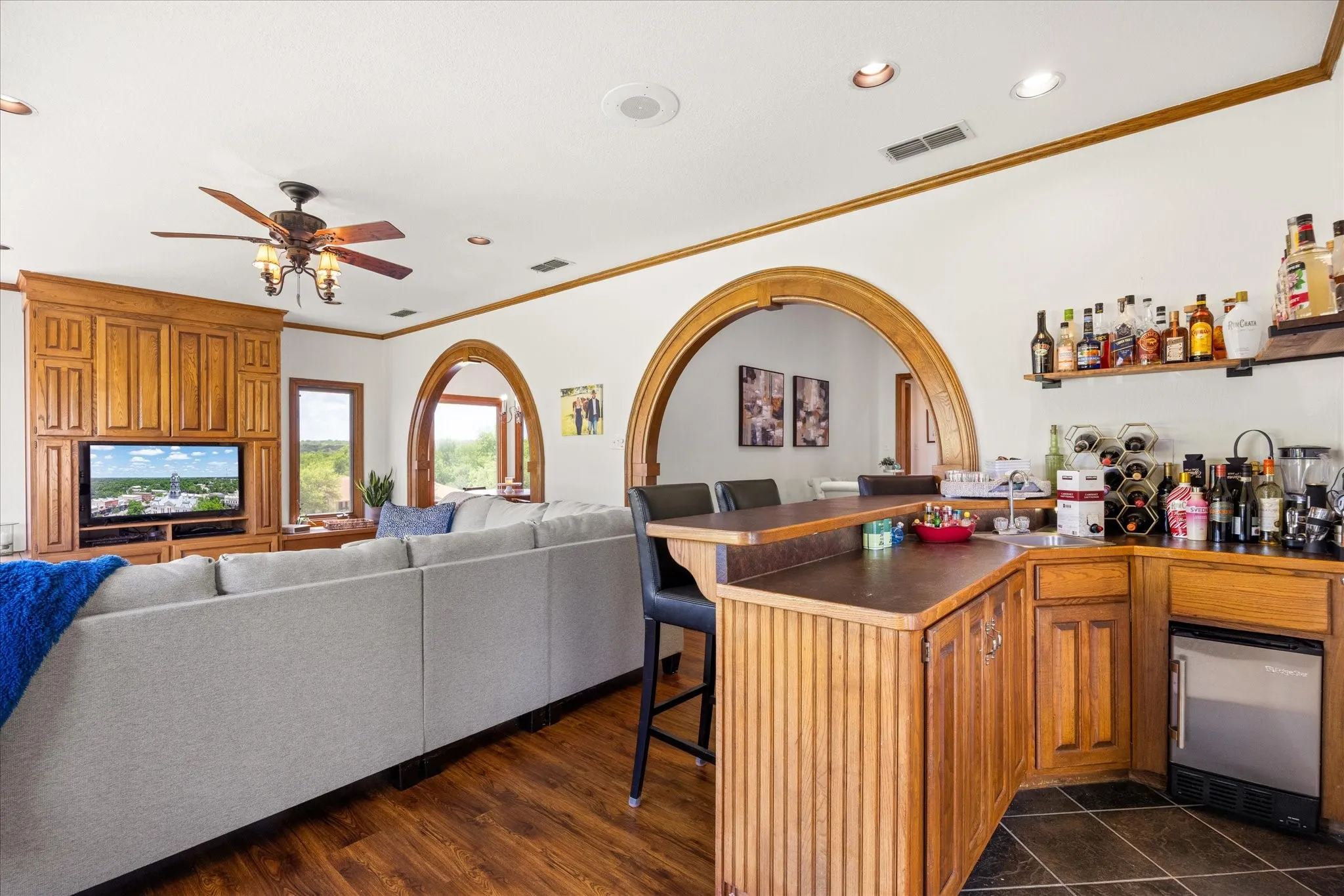 Indoor wet bar featuring dark countertops, wood finish cabinetry, stainless steel refrigerator, recessed lighting, and crown molding