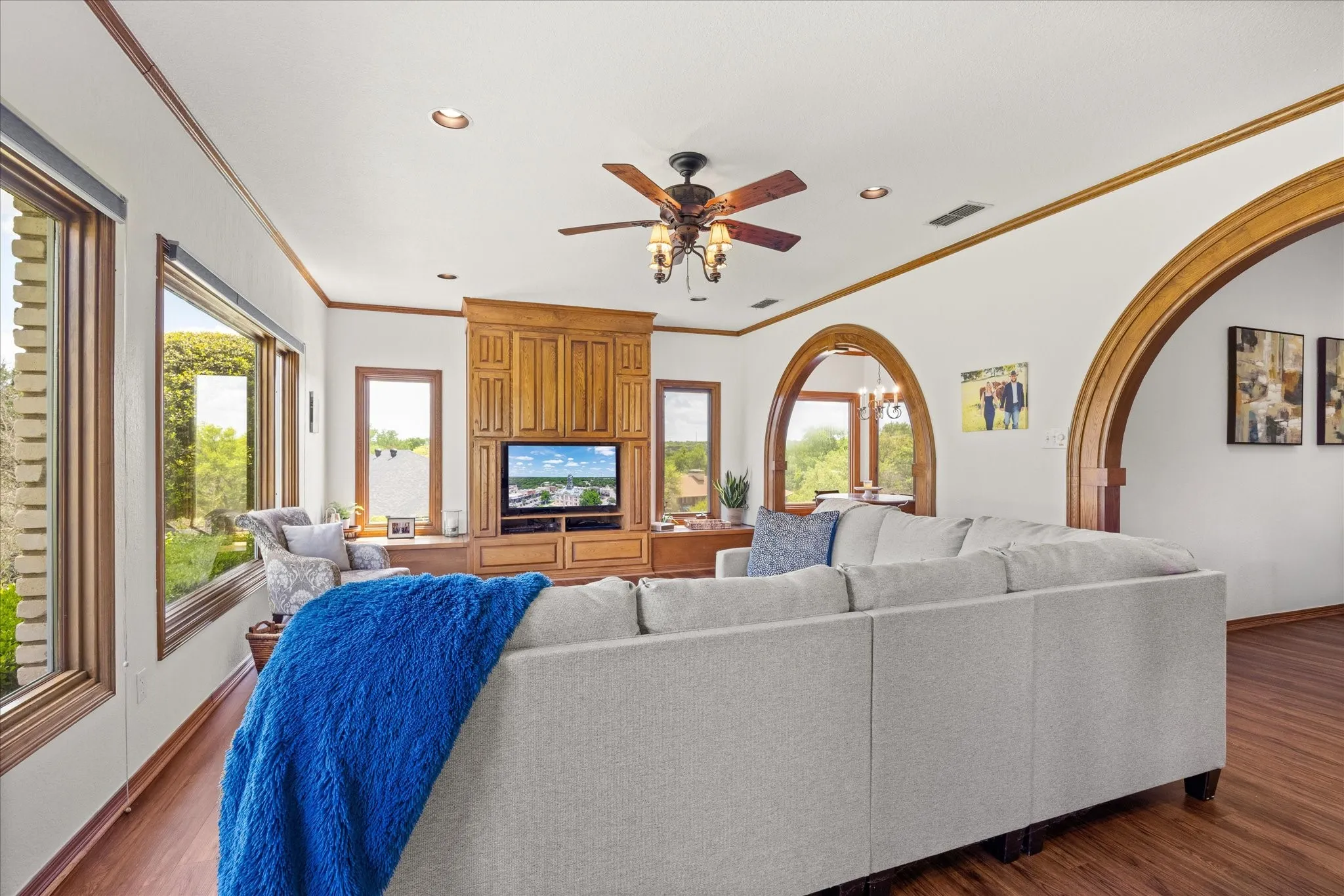 Living room with ceiling fan, dark wood-style floors, crown molding, arched walkways, and a chandelier