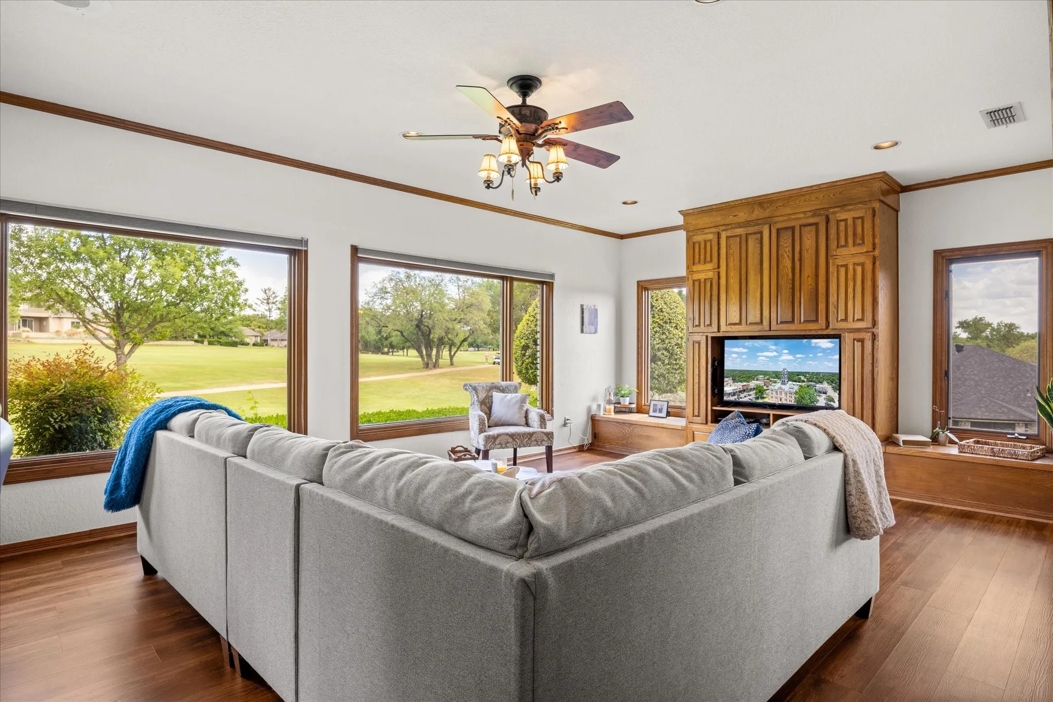 Living room with ceiling fan, dark wood-type flooring, ornamental molding, view of golf course, and recessed lighting