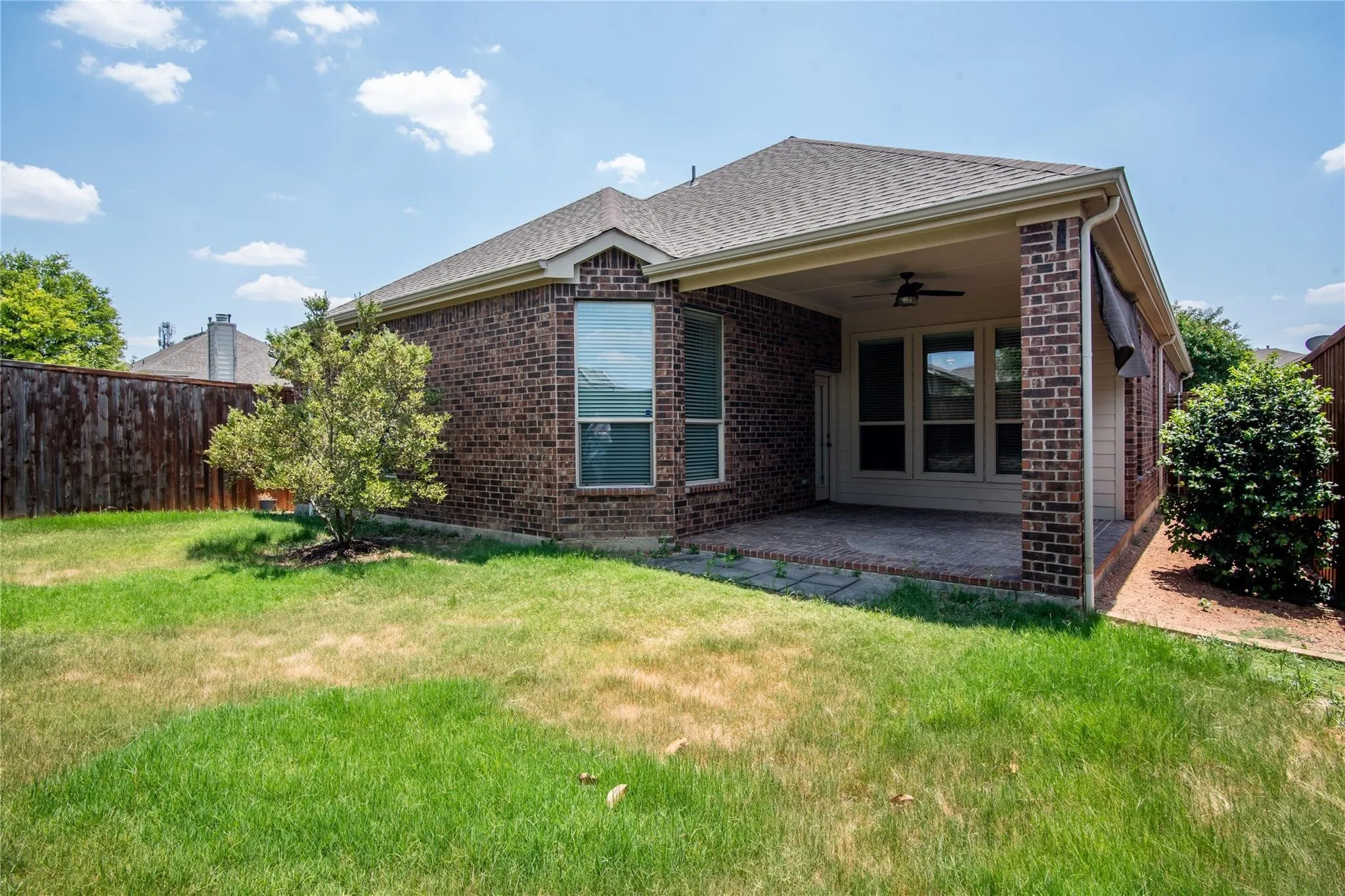 Rear view of house with brick siding, a ceiling fan, a patio area, and roof with shingles