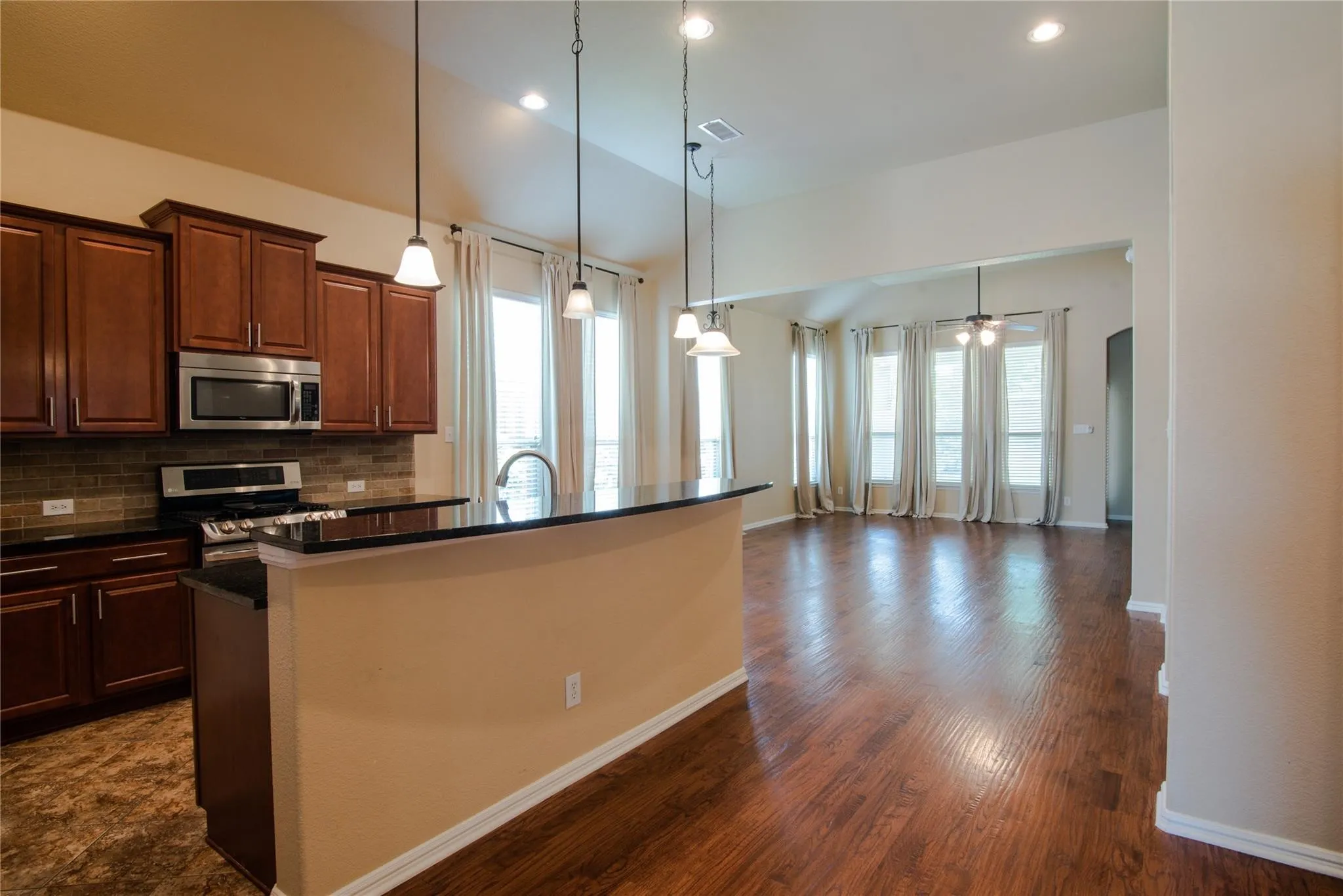 Kitchen featuring stainless steel appliances, a kitchen island with sink, pendant lighting, a ceiling fan, and dark stone counters