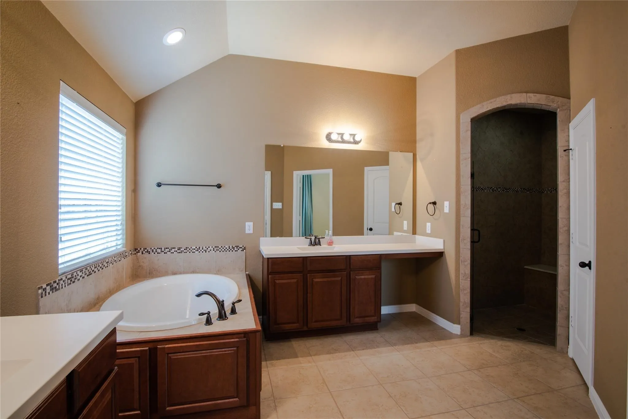 Bathroom featuring vanity, vaulted ceiling, a stall shower, a bath, and light tile patterned floors